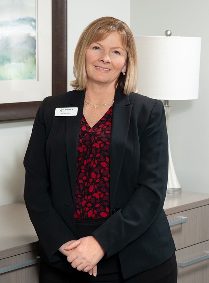 Woman in a black blazer and red floral top, smiling, standing in an office.