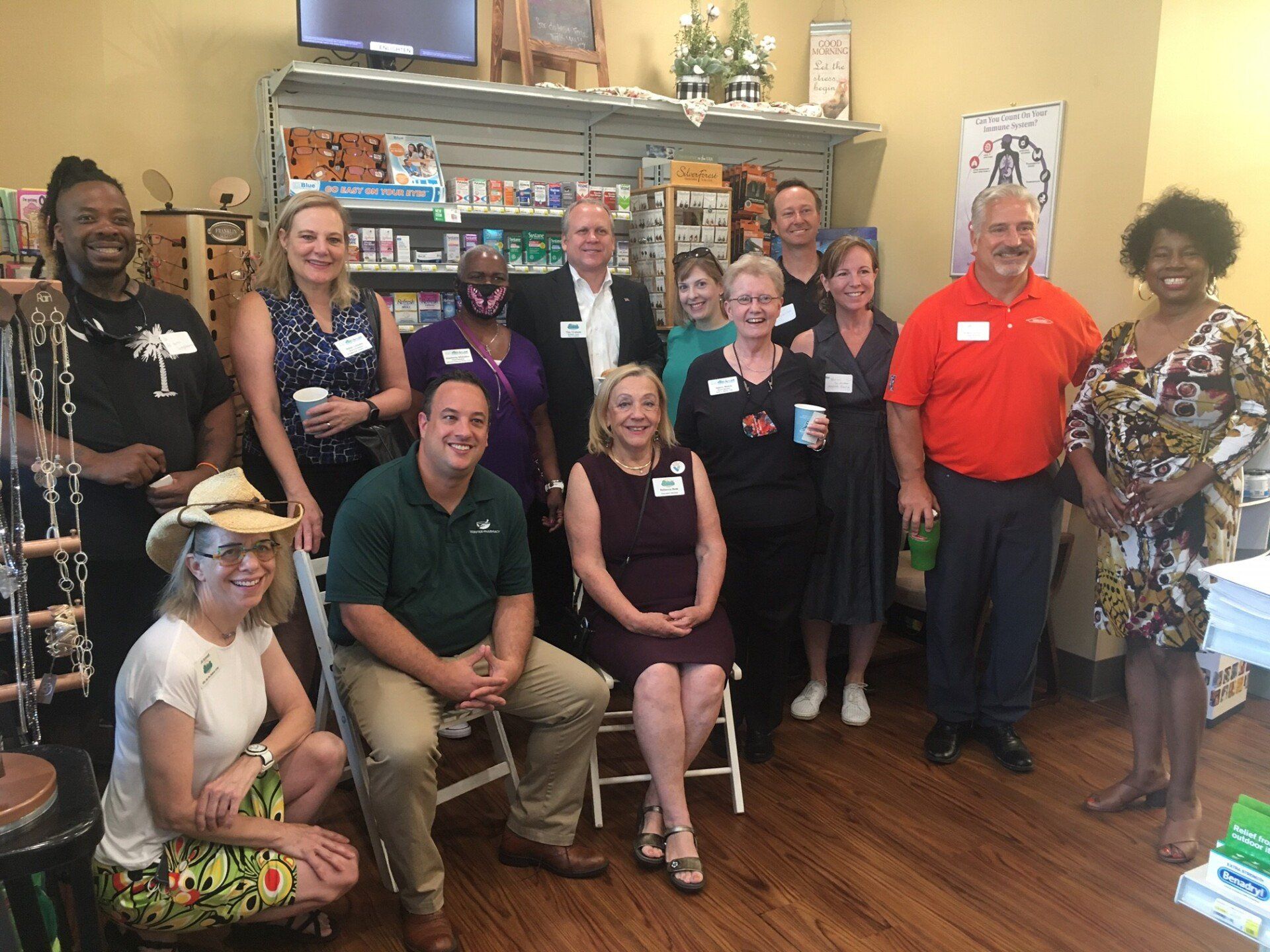 Group of people inside a shop; smiling, posing, and holding drinks; shelves with products in background.