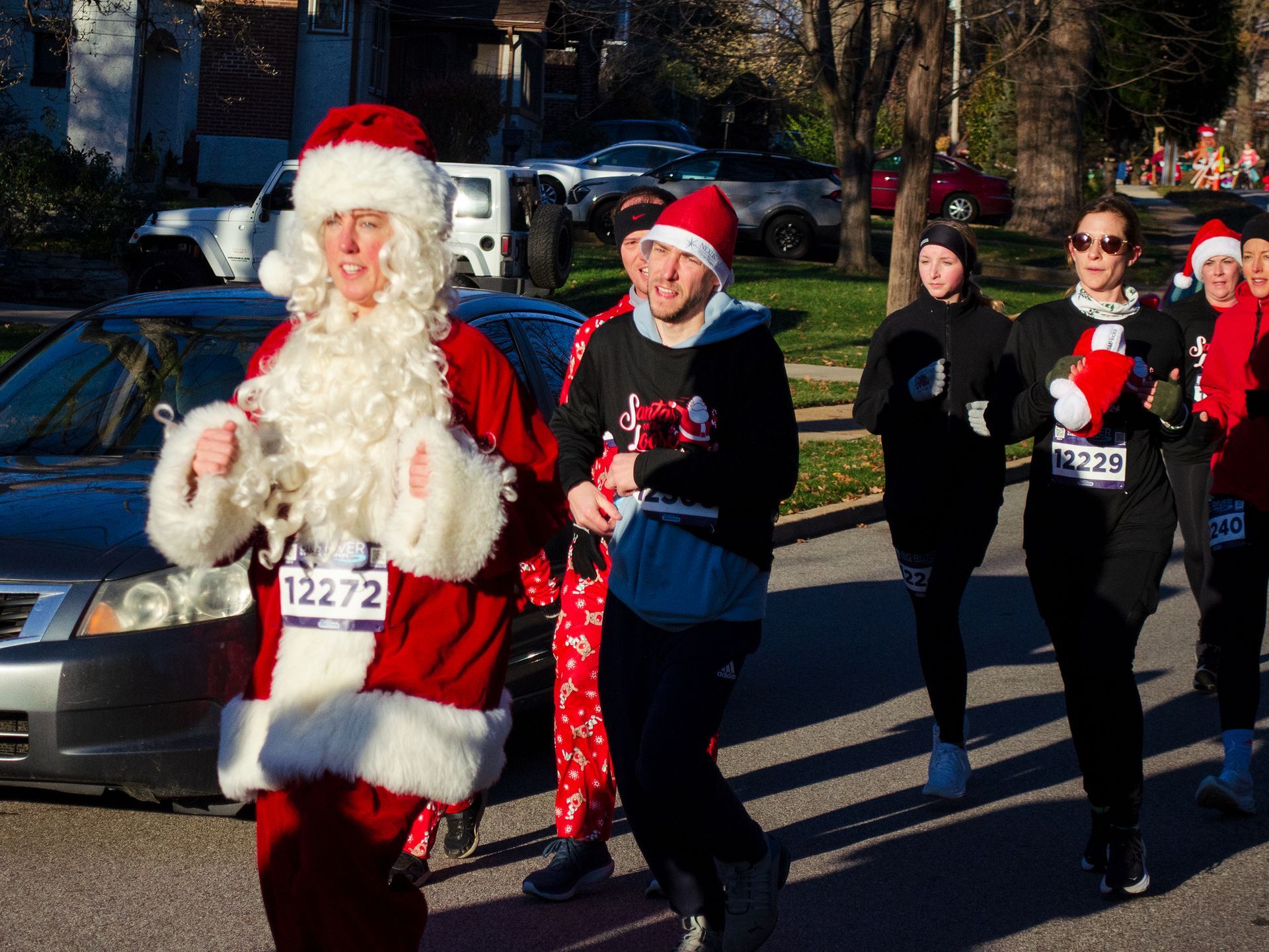 People in Santa costumes running on a street; sunny day.