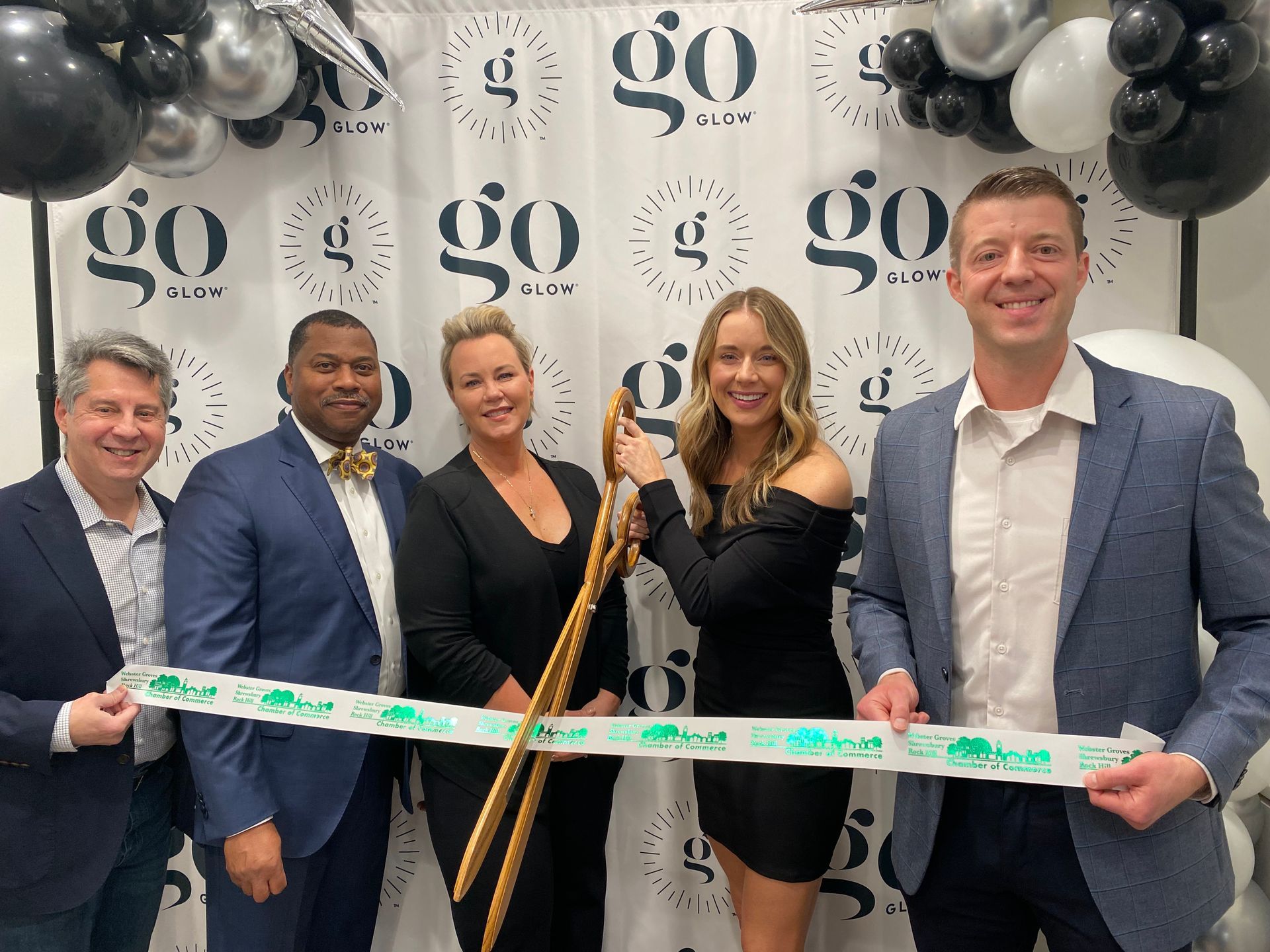 People cutting ribbon at an opening event; balloons in background.