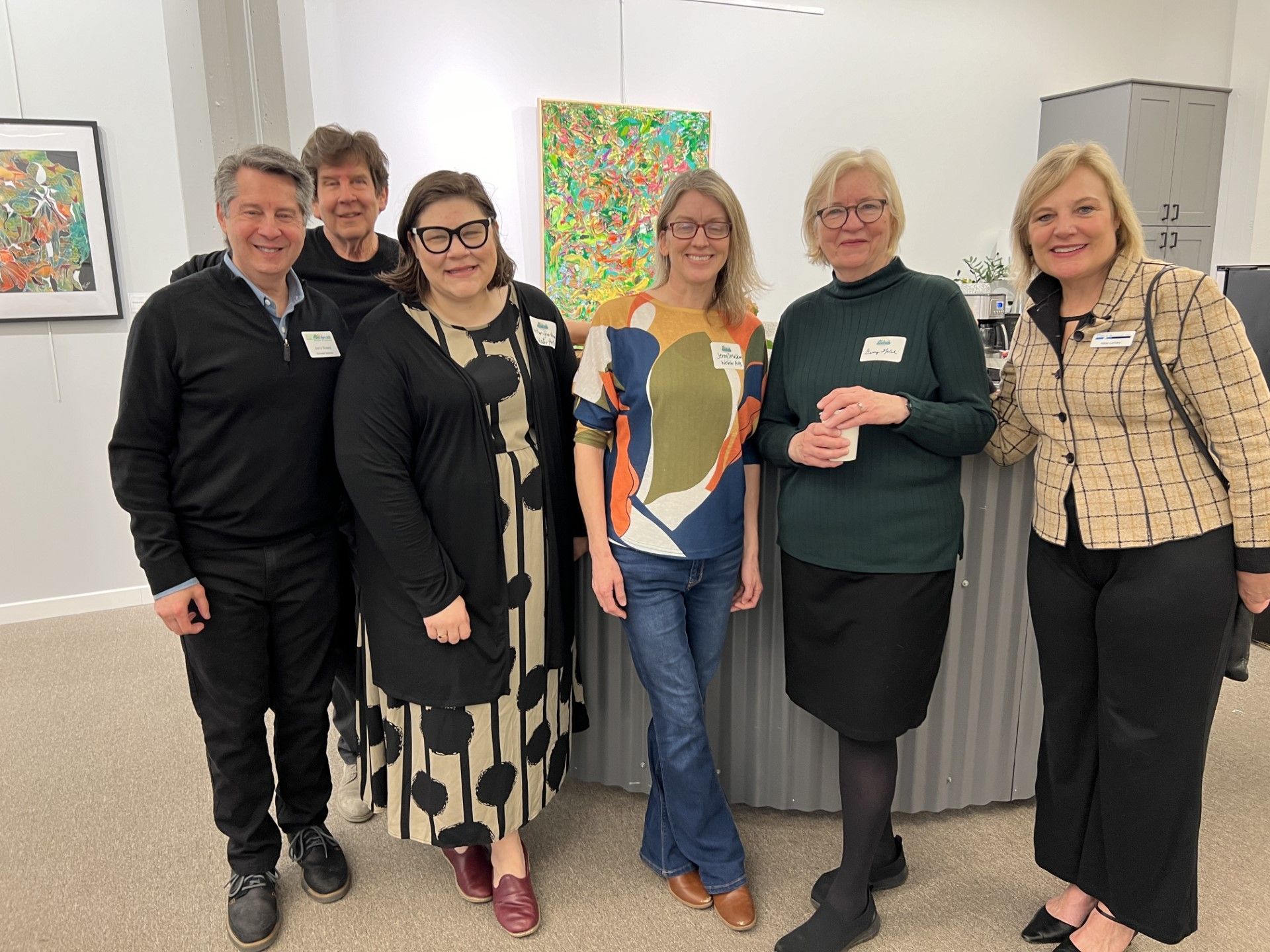 Group of people at an art gallery, smiling and posing near a colorful painting.