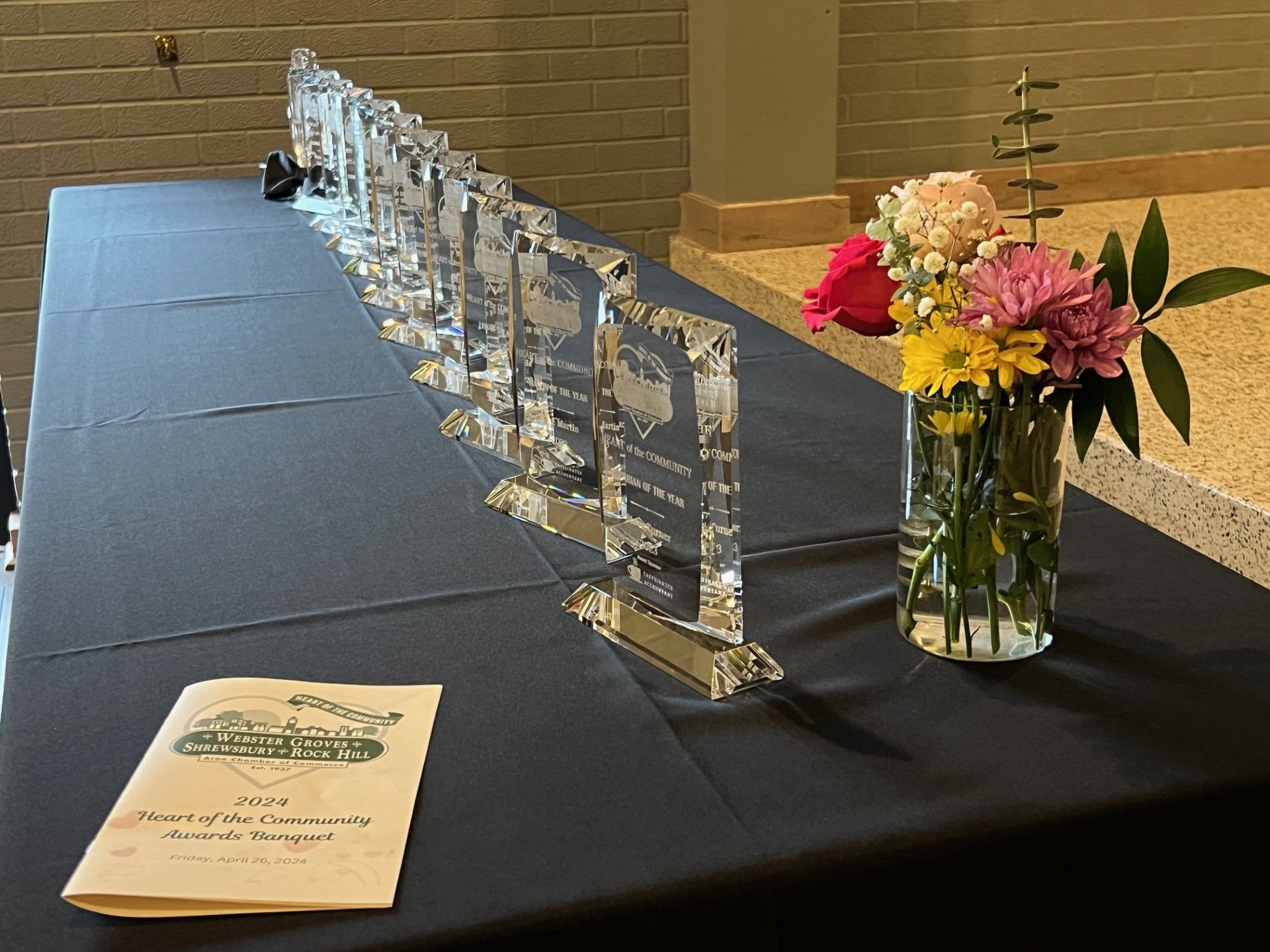 Table with trophies and flowers; event program on left. Black tablecloth, neutral background.
