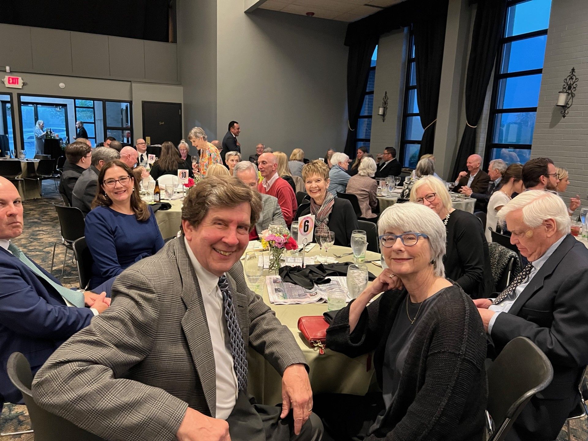 People seated at tables in a banquet hall, smiling, and looking at the camera.