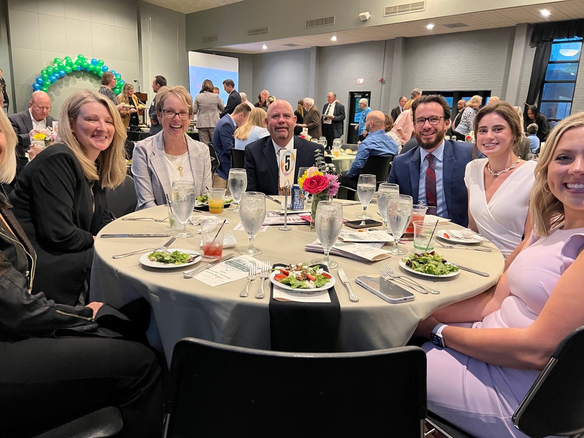 People seated around a round table at an event, with food and drinks.