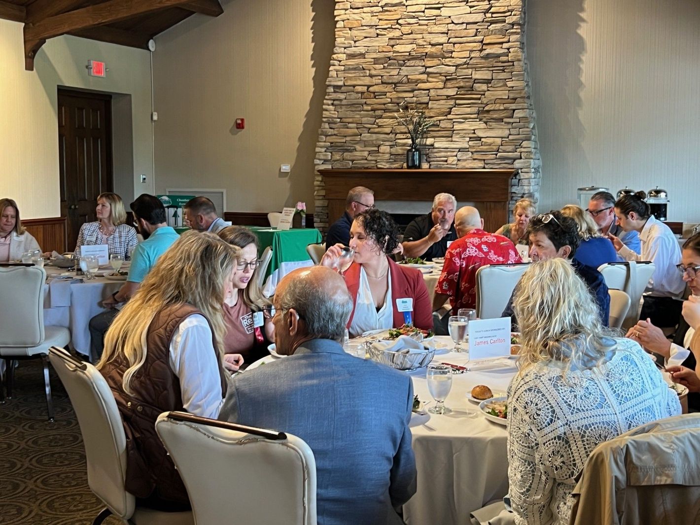 People seated at round tables in a restaurant, a stone fireplace in the background.