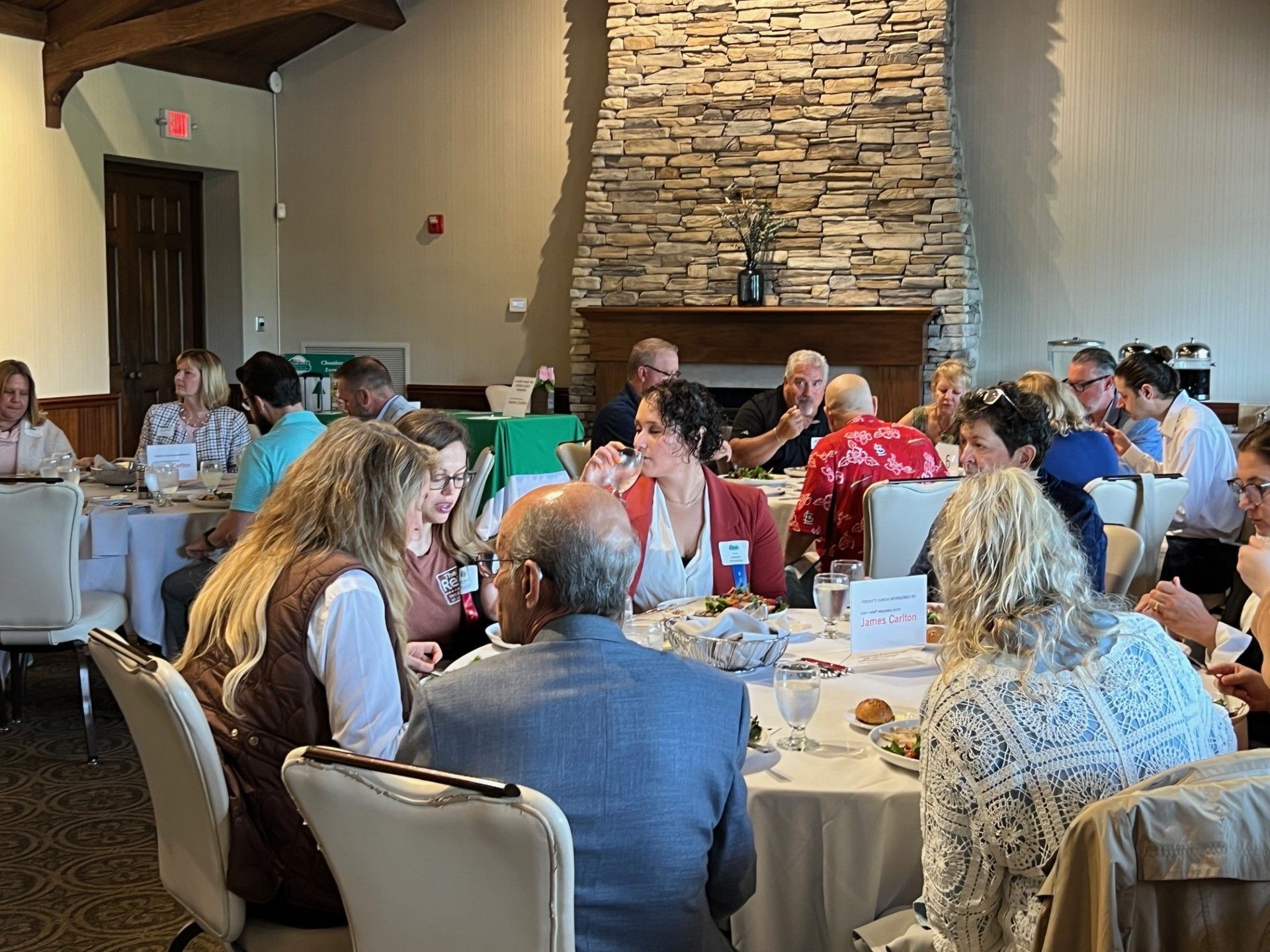 People seated at round tables in a restaurant, a stone fireplace in the background.