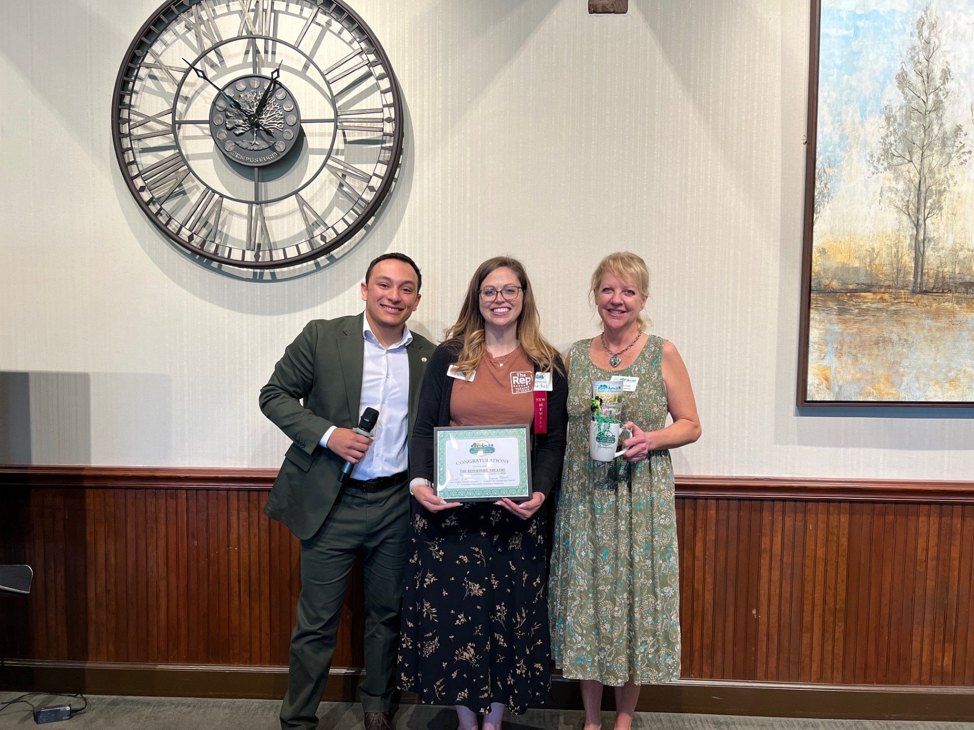 Three people stand holding awards in front of a clock and artwork.