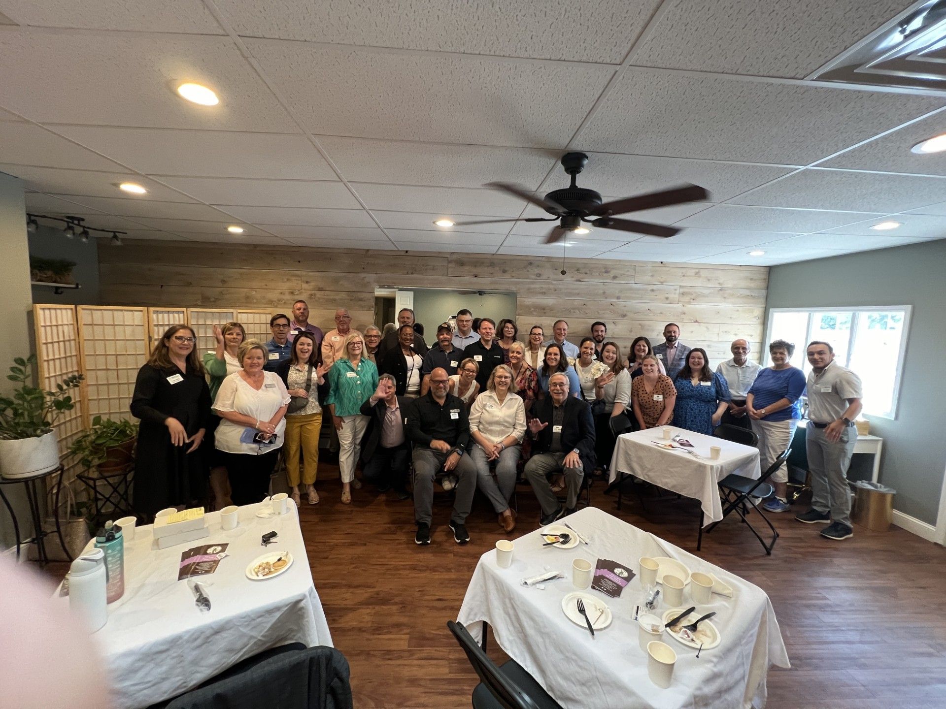 Large group of people gathered indoors near tables with food and promotional materials.