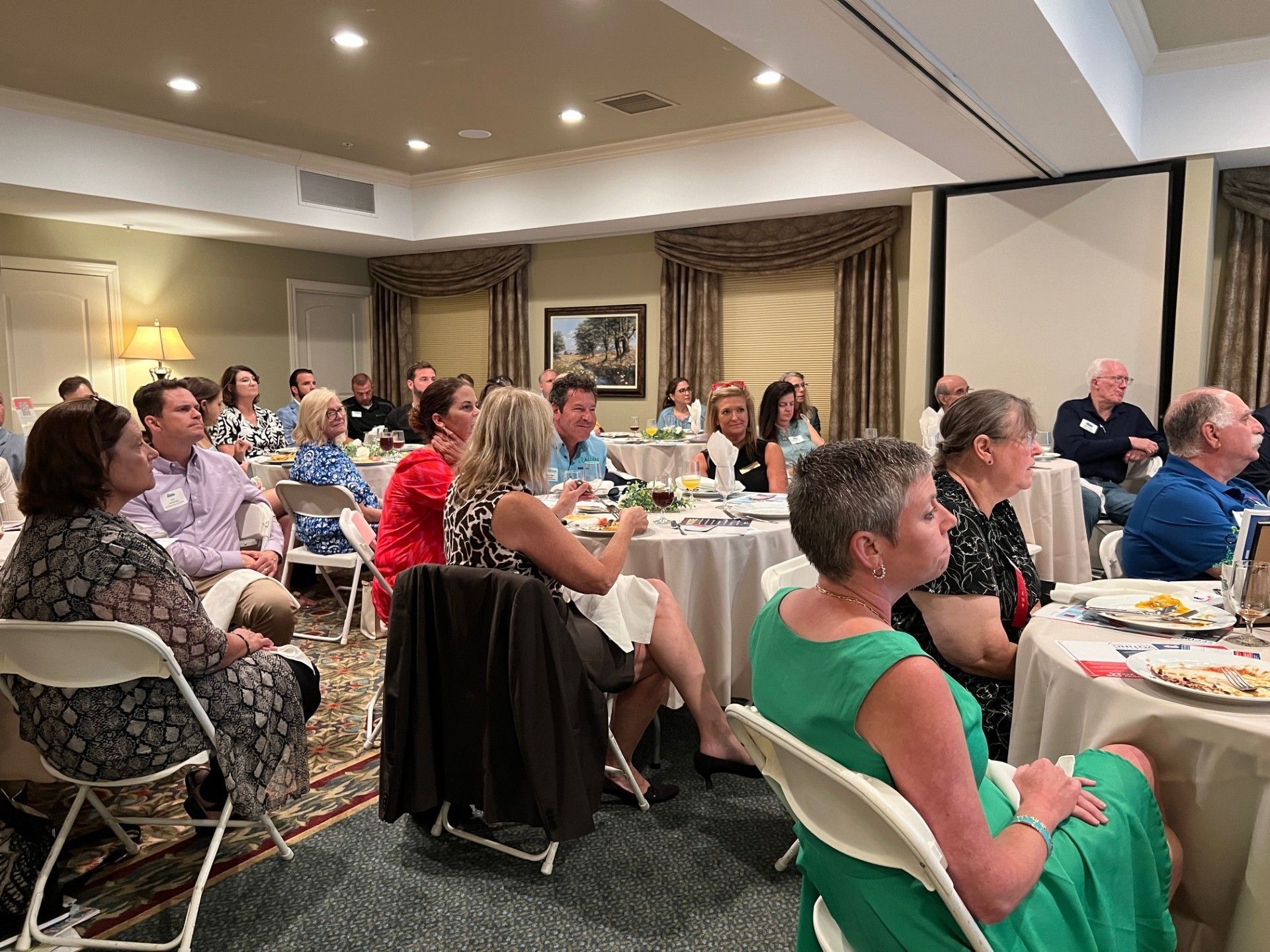 People seated at tables in a brightly lit room, attending a meeting or presentation.