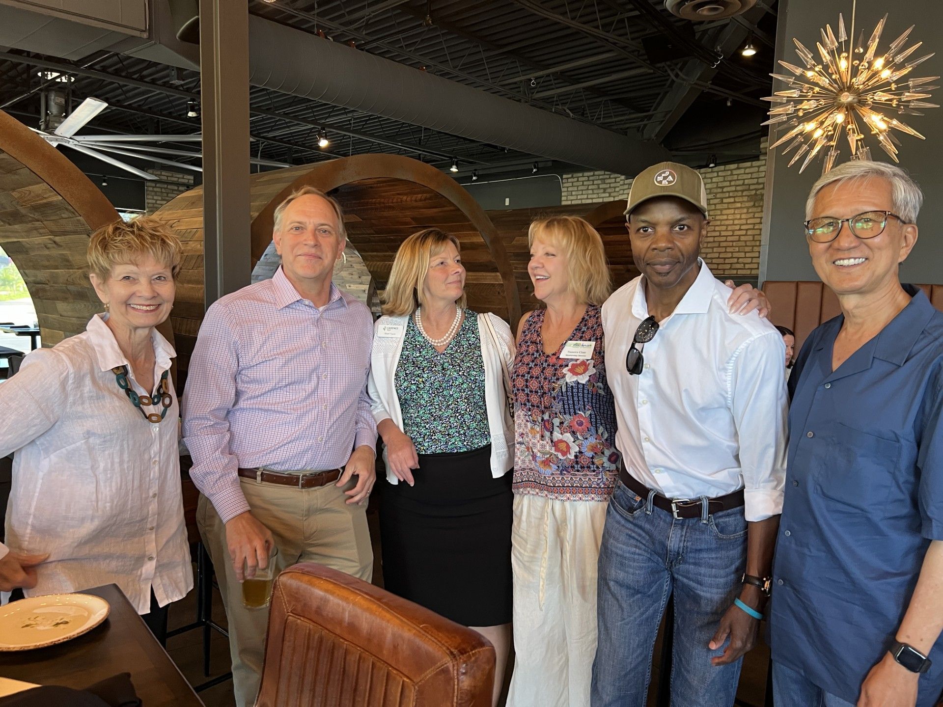 Group of people smiling, posing for photo inside restaurant. Some are wearing casual clothing.