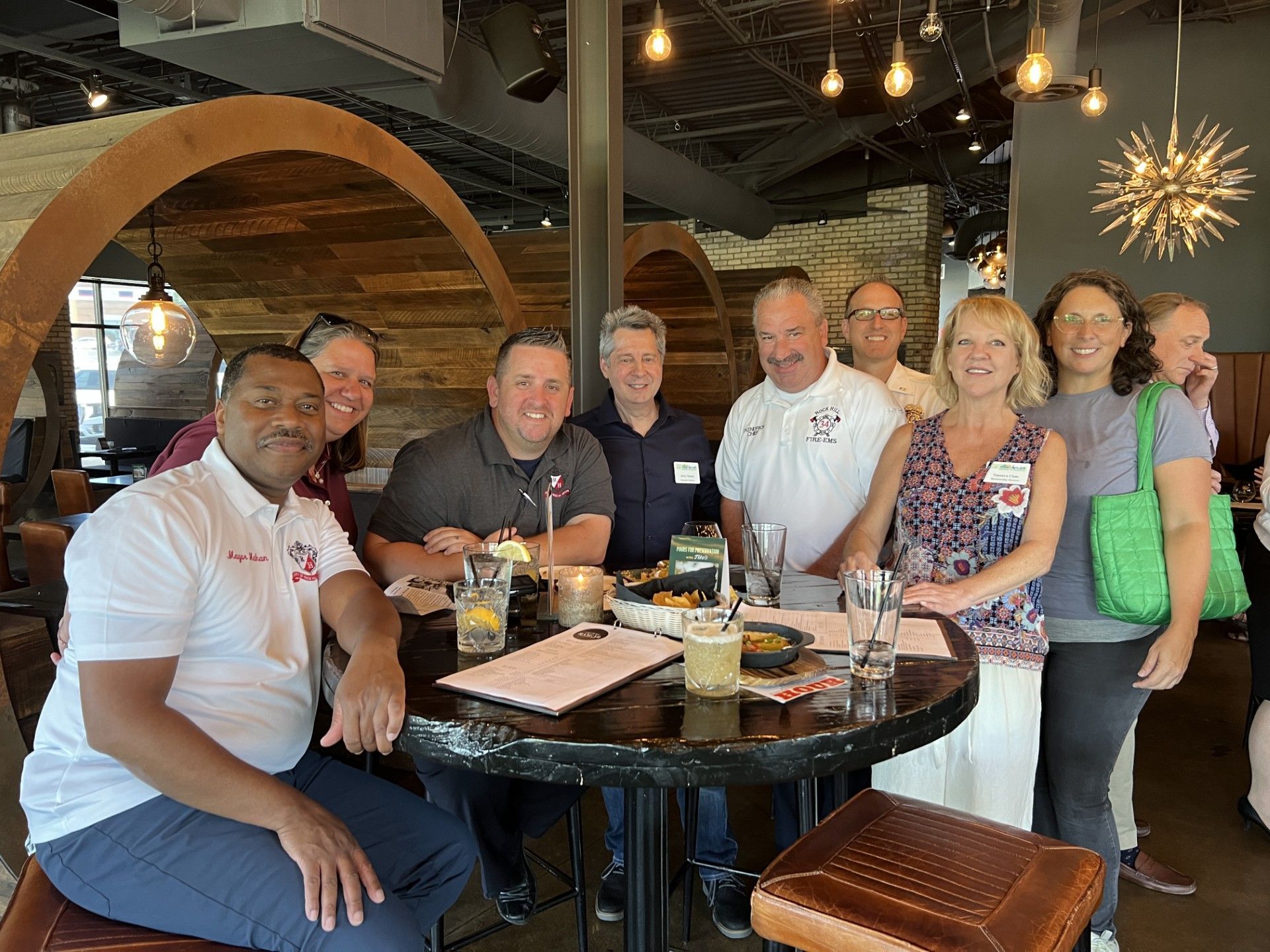 Group of people gathered around a round table in a restaurant. People are smiling and socializing.
