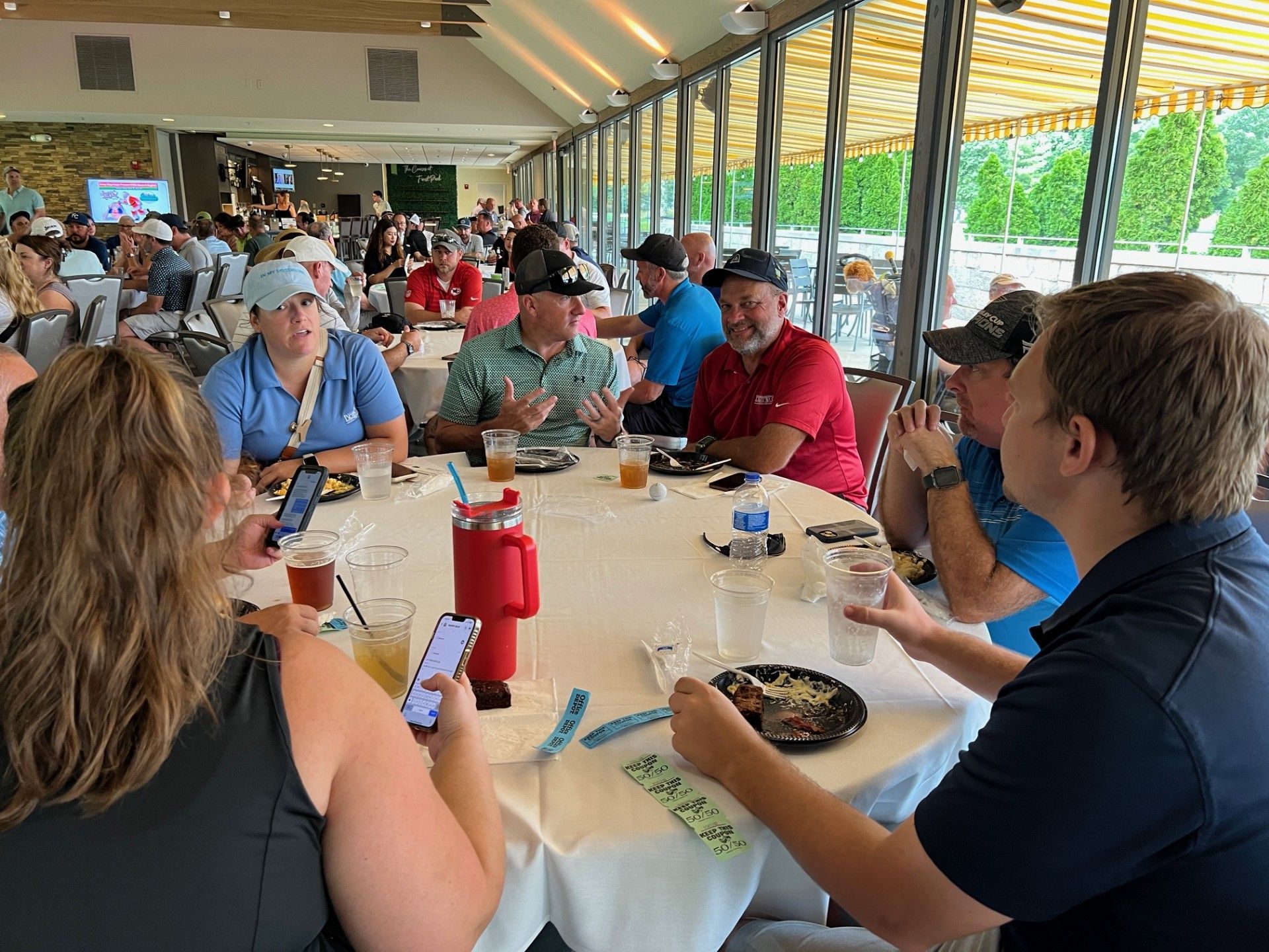 People seated around a white round table, chatting, eating, and looking at phones inside a dining area.