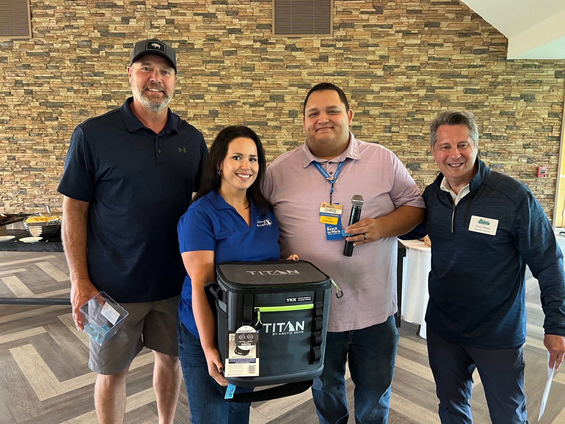 Four people standing, smiling, holding a cooler, inside a room.