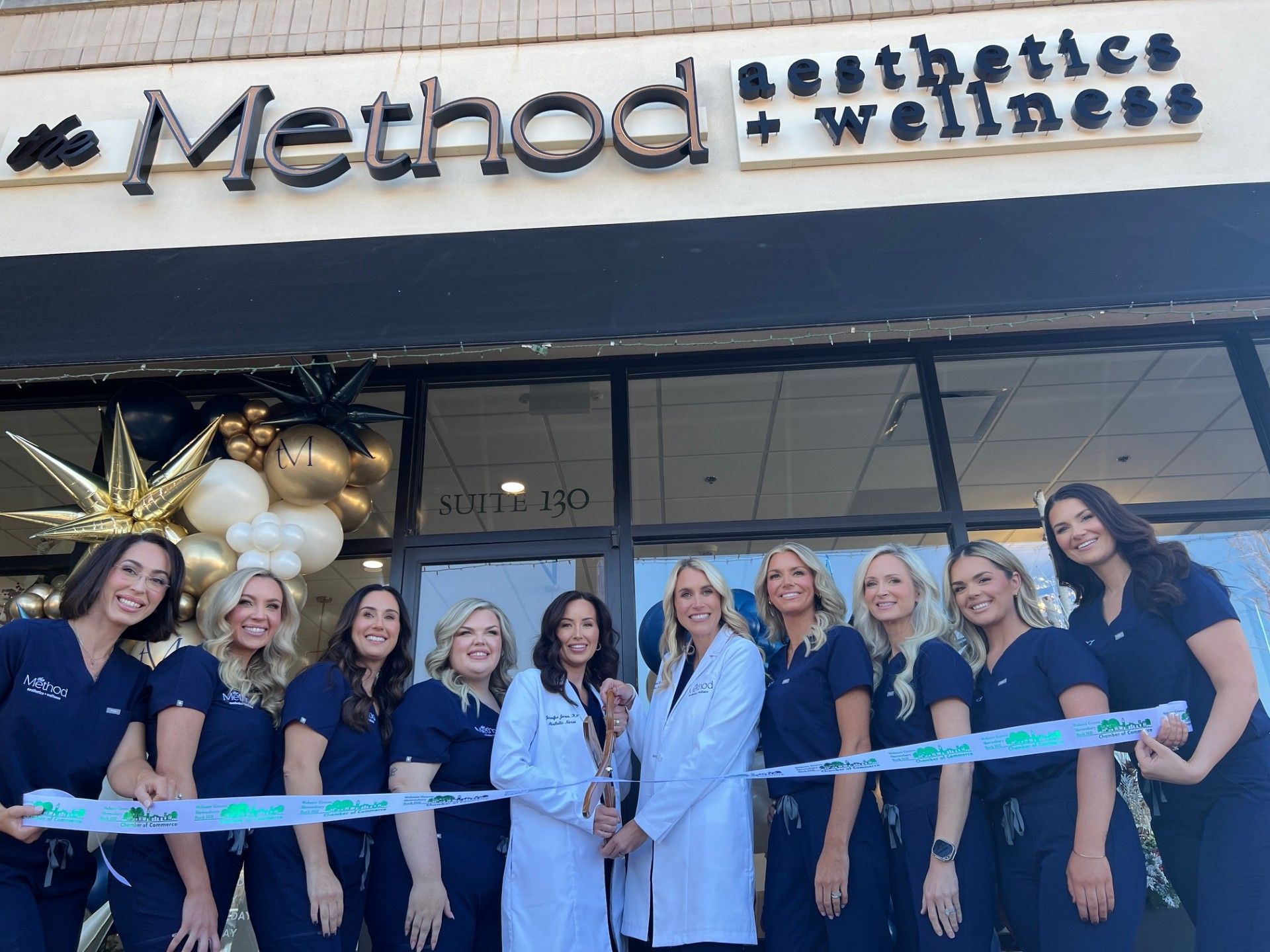 Ribbon-cutting ceremony at Method Aesthetics + Wellness. Group of staff in scrubs cuts a ribbon outside a storefront.