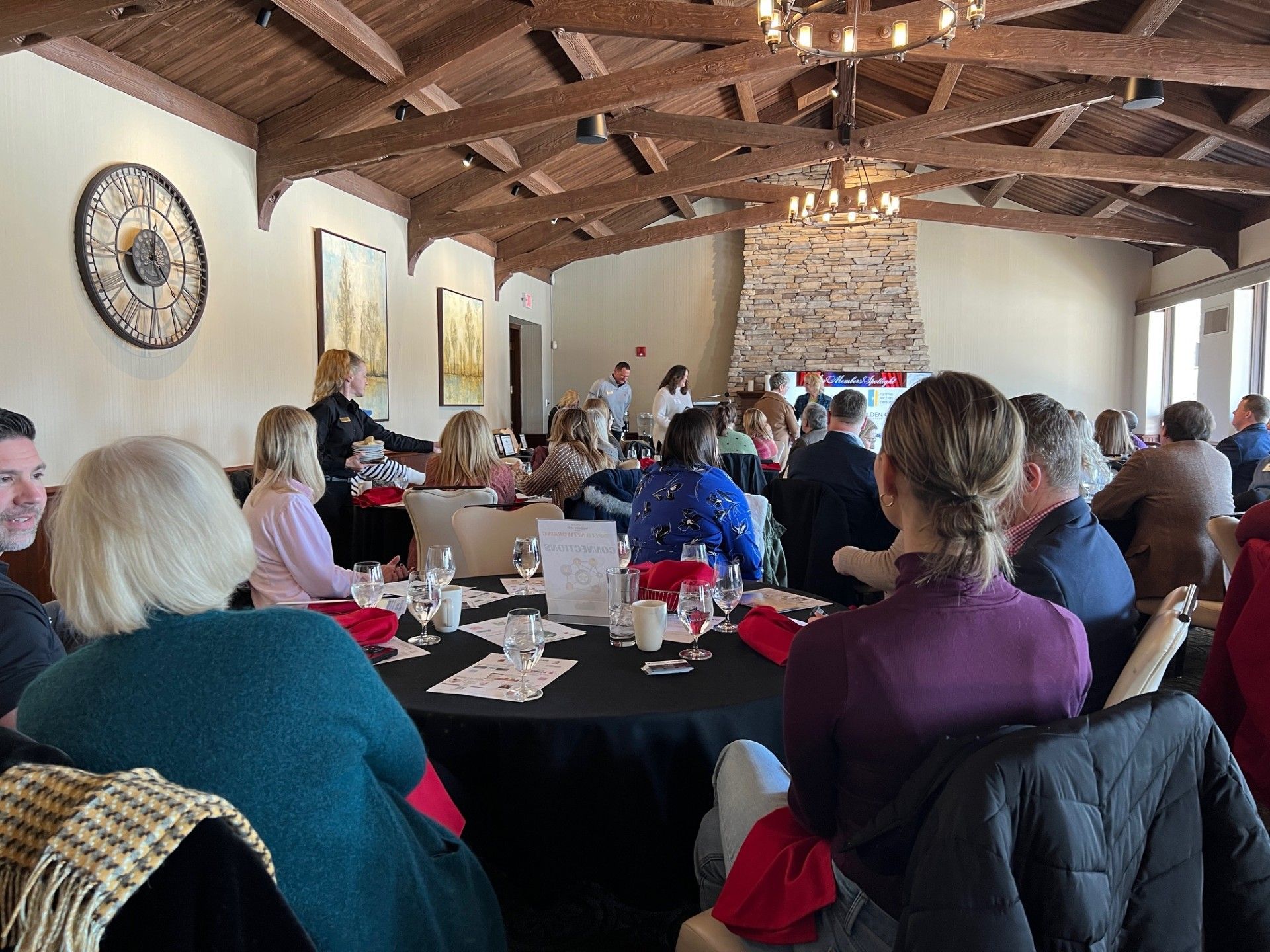 People seated at round tables in a restaurant, attending a presentation.