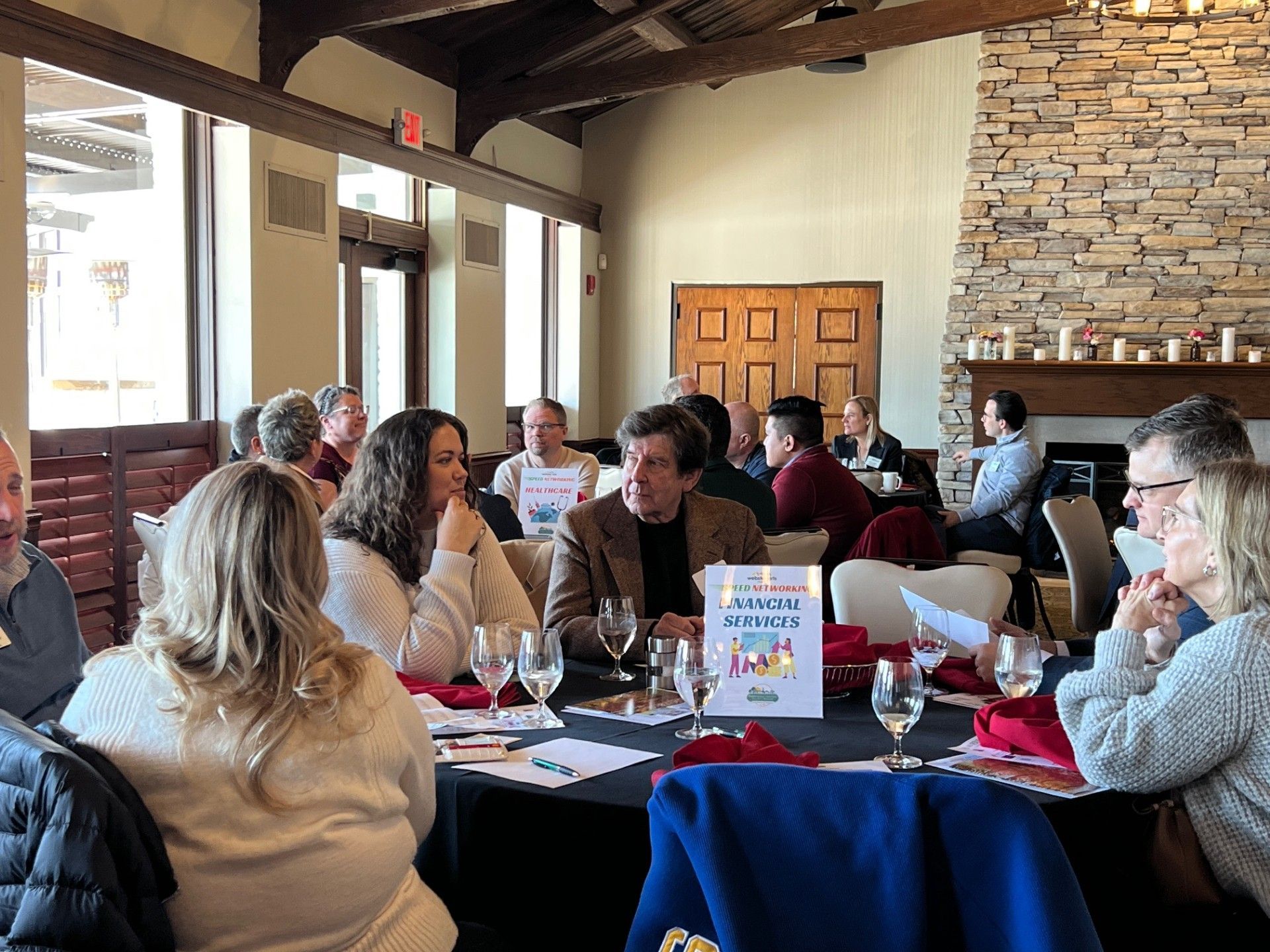 People seated at tables in a restaurant, possibly for a meeting. Some are talking, others look at papers.