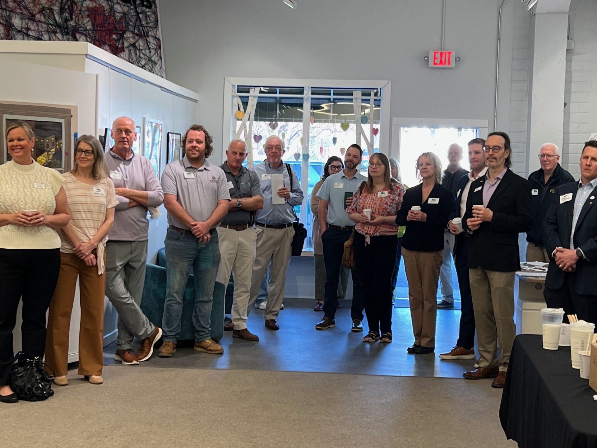 Group of people inside an art gallery, standing and looking forward. Some hold drinks.
