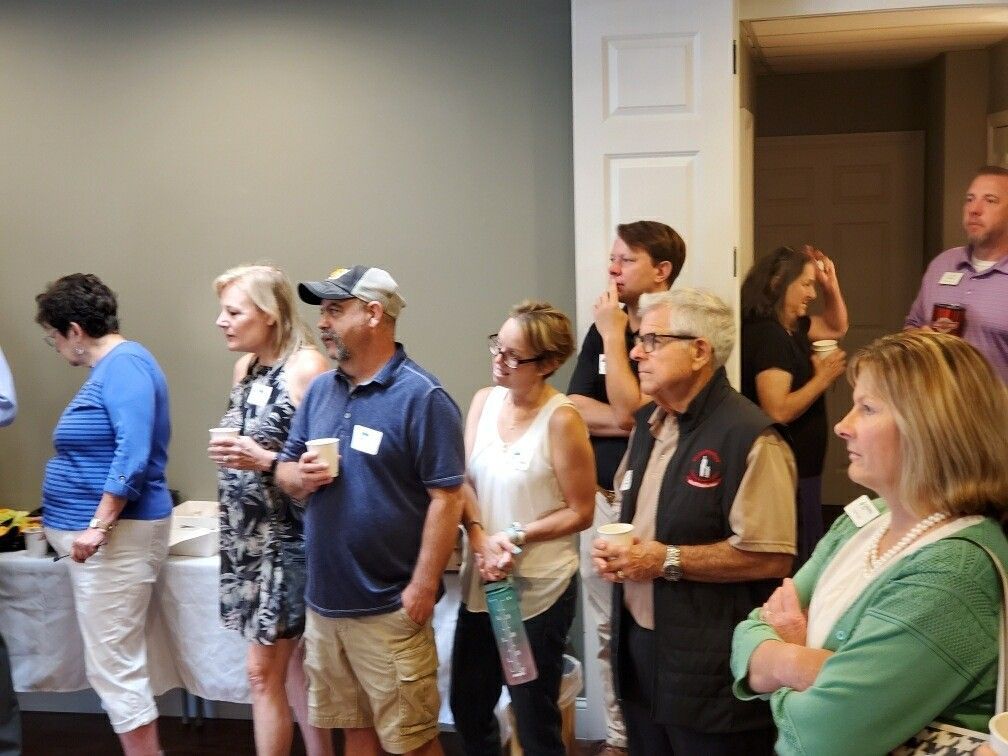 People at an event, some holding cups. They are looking to the side. Light colors, indoors.