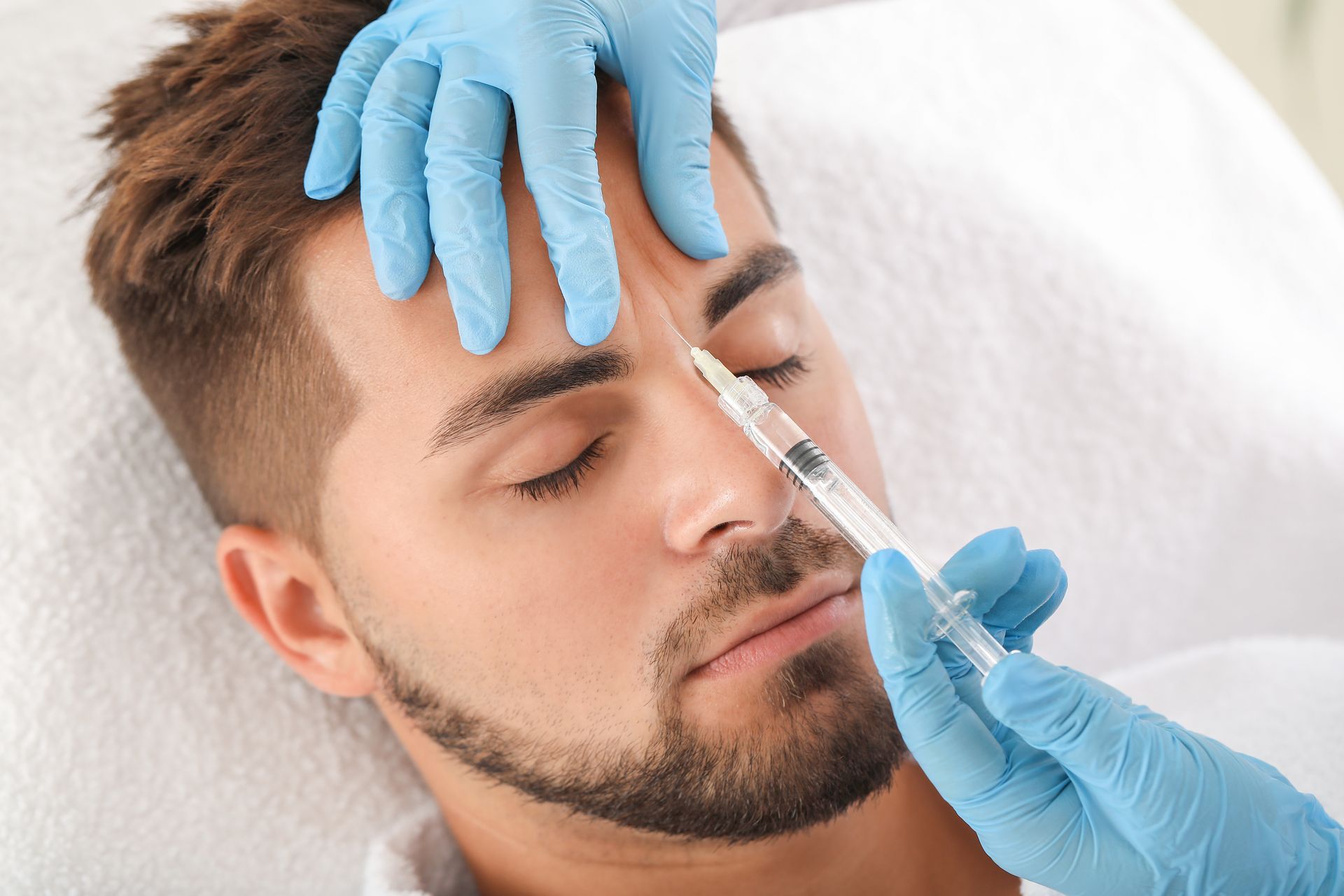 Man receiving an injection to the forehead. Medical professional in blue gloves holds syringe.