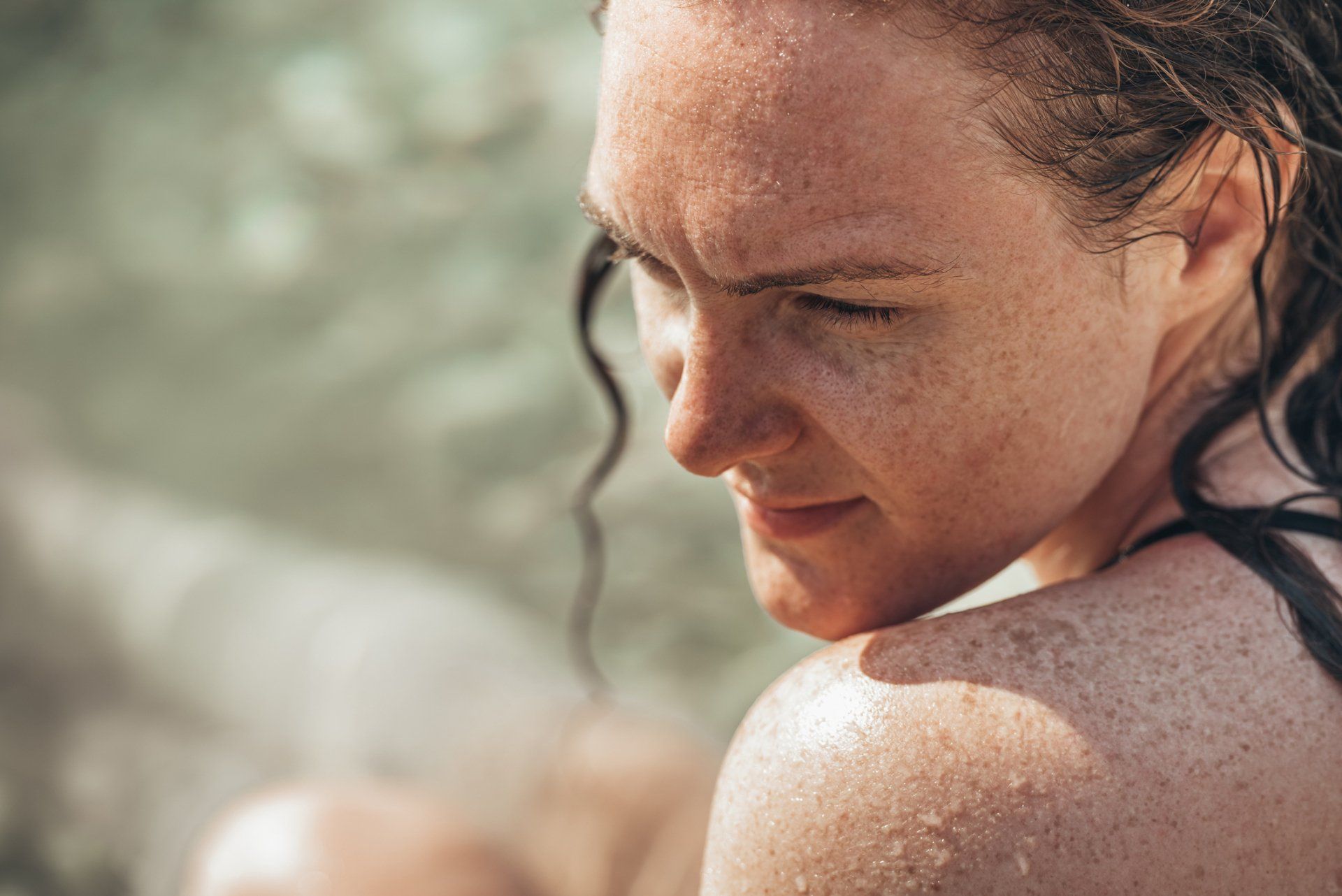 Woman with wet skin and freckles looking to the right, against a blurred background.
