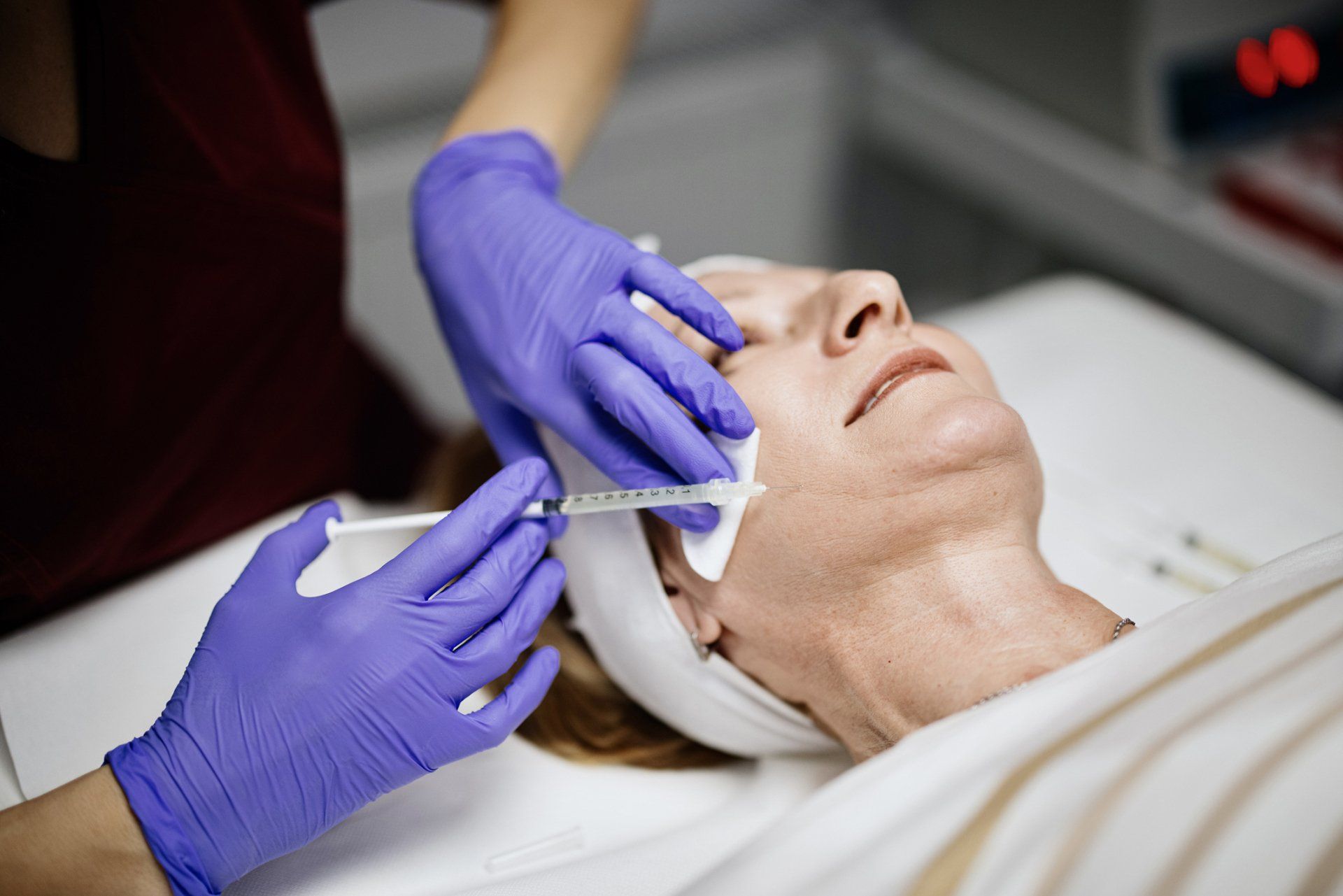 Person receiving facial injections by gloved hands, medical setting.
