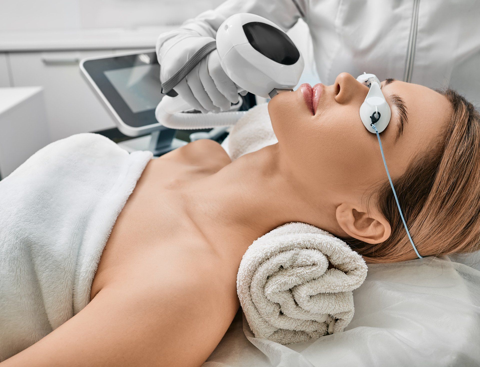 Woman receiving a facial laser treatment, lying down with eye protection.
