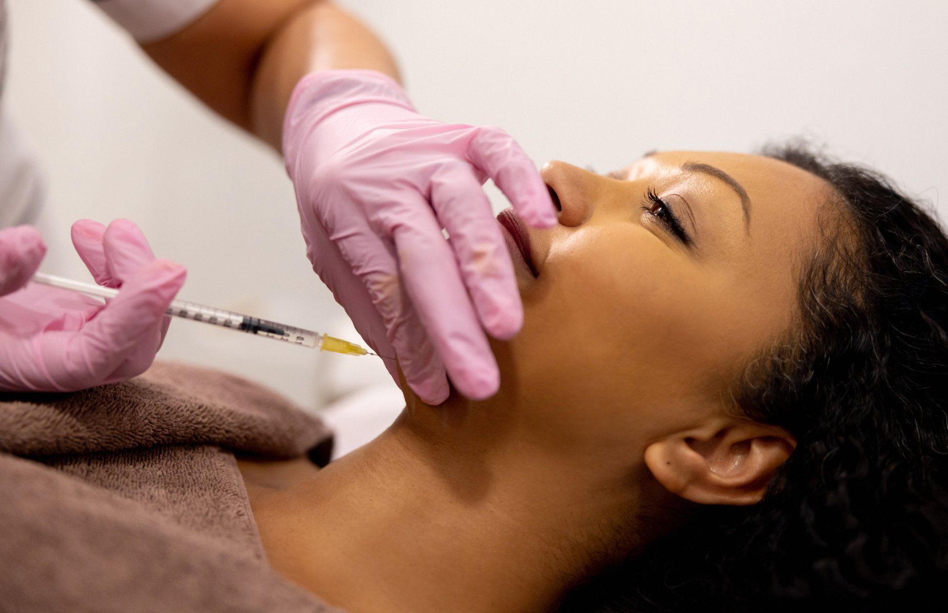 Cosmetic injection procedure A person receiving an injection in the chin area from a gloved hand.