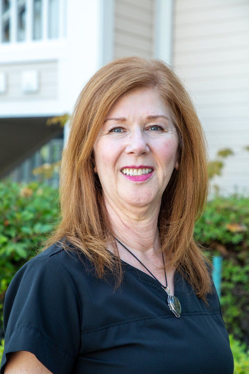 Woman with red hair smiling, wearing a black top, outdoors near a building.