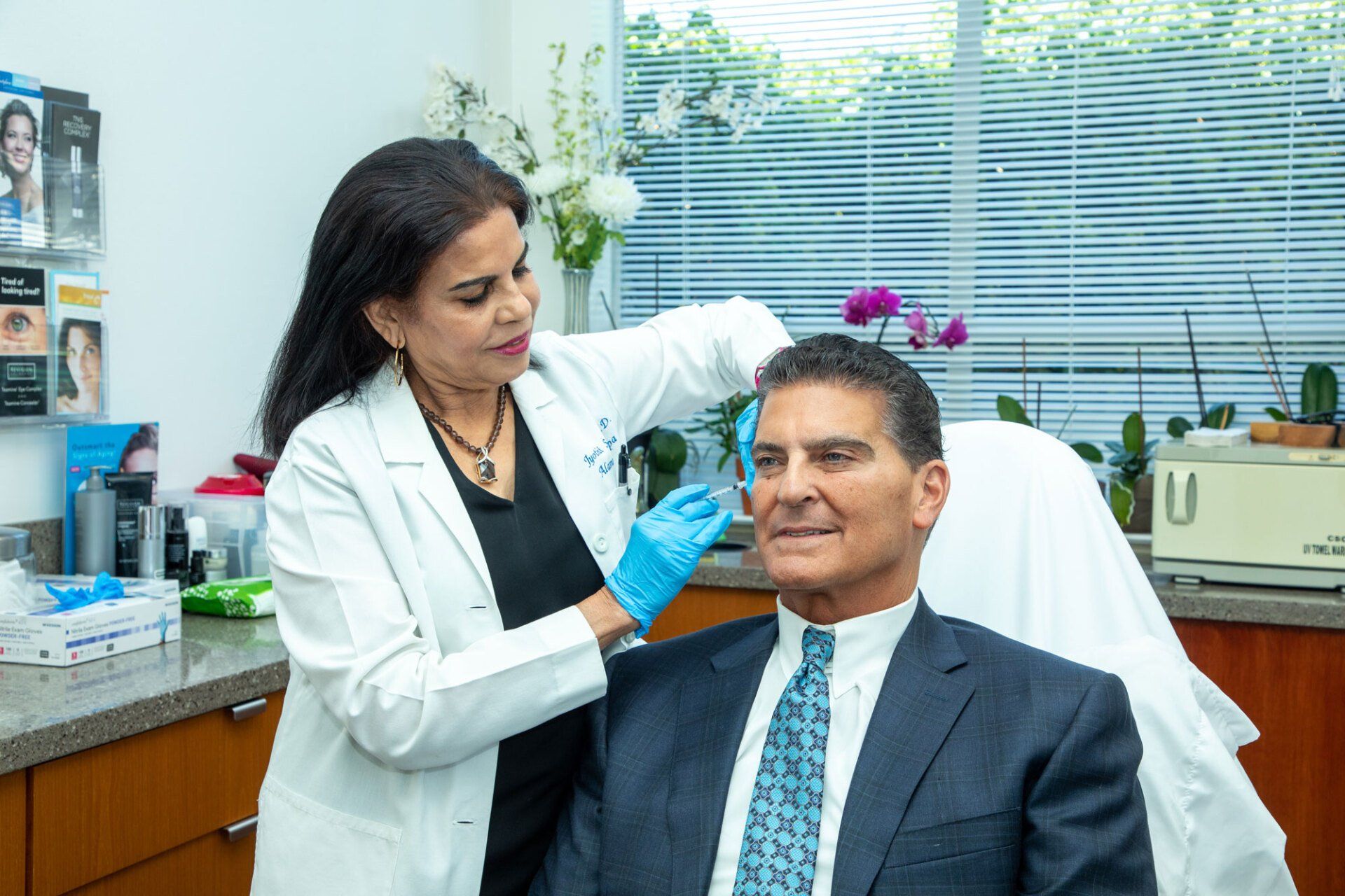 A medical professional in a lab coat giving a facial injection to a man in a suit, in a clinic setting.