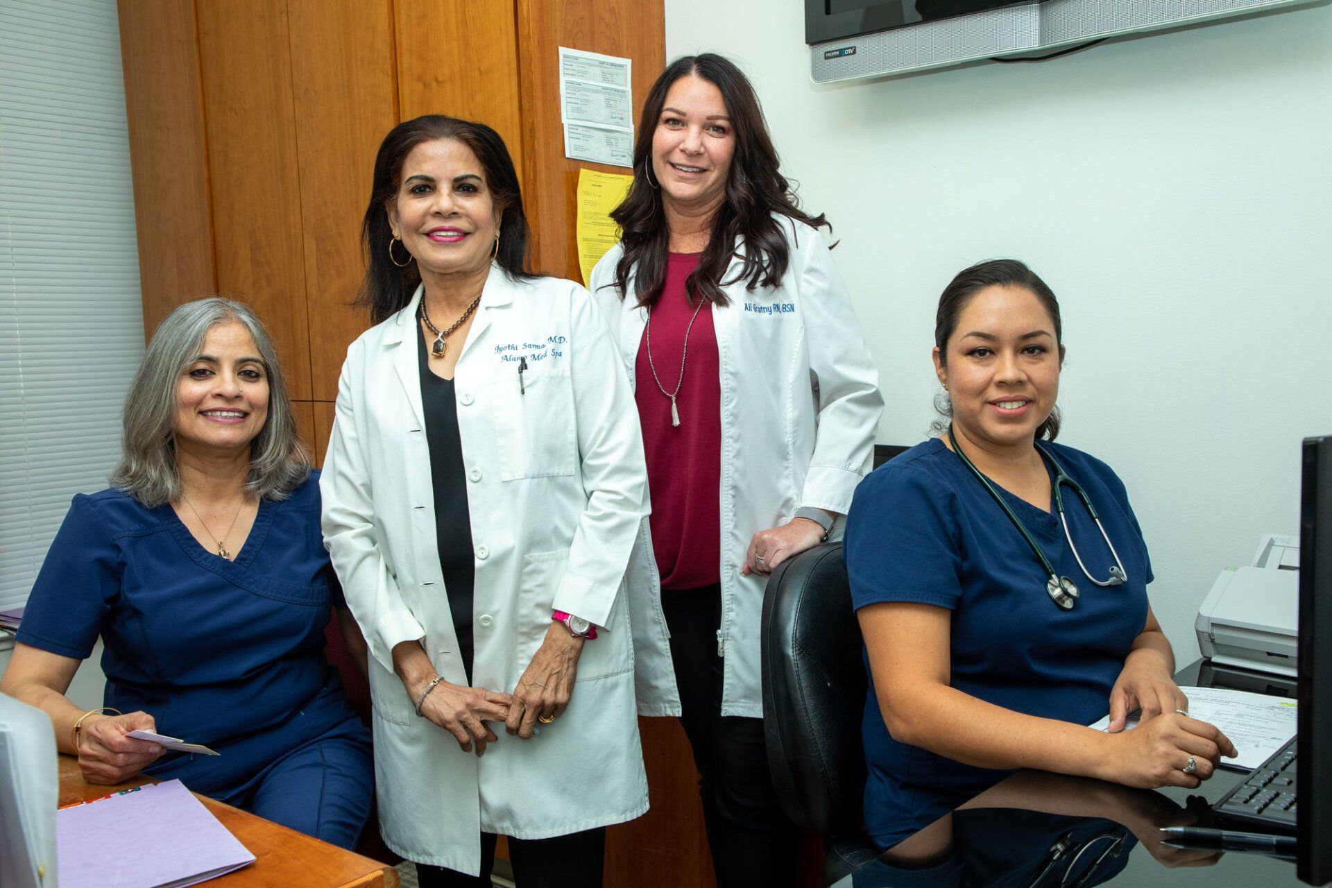 Alamo MD MedSpa Staff Four healthcare workers in scrubs and lab coats smiling in an office.