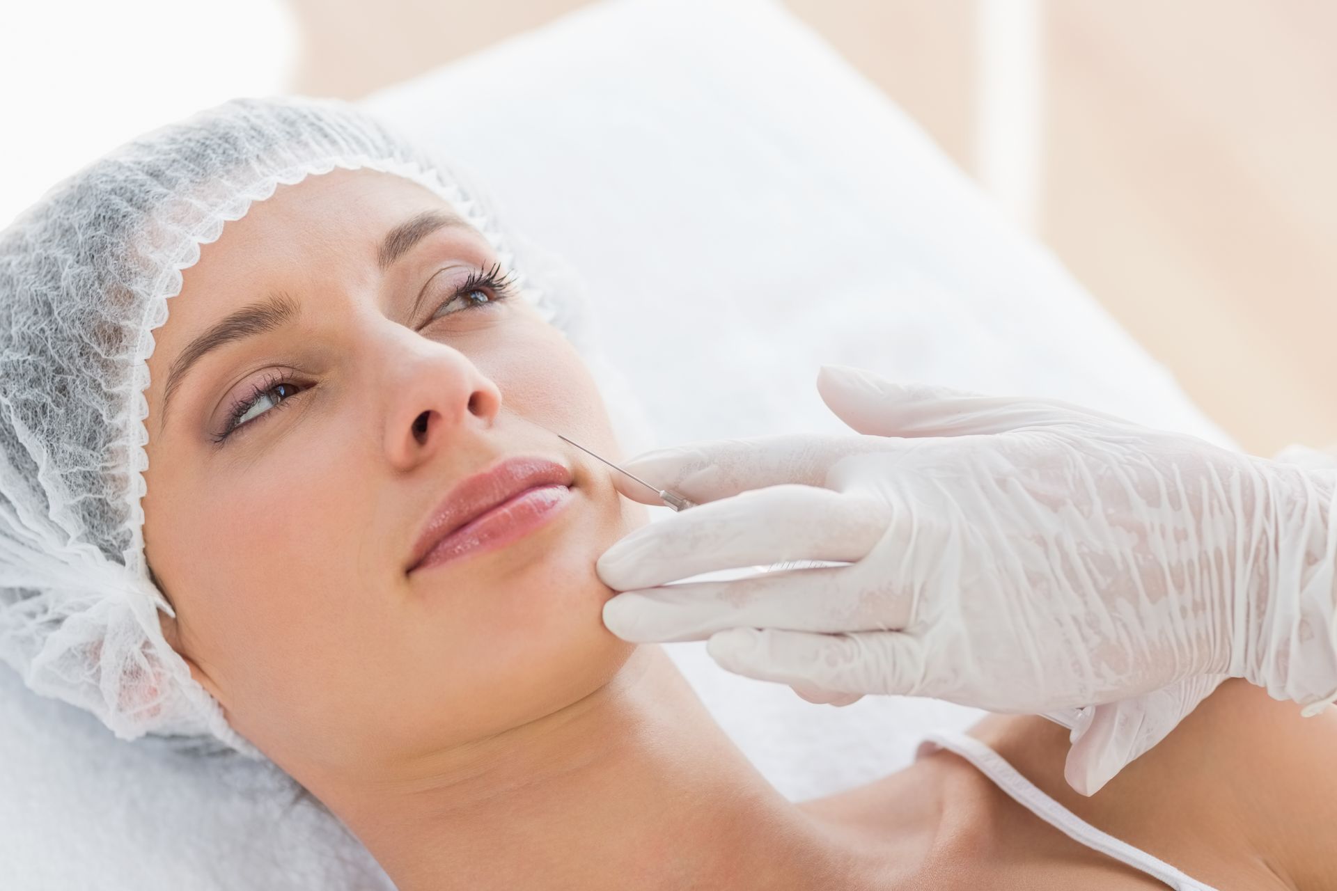 Gloved hands performing a skincare treatment on a client at a professional spa clinic treatment area.