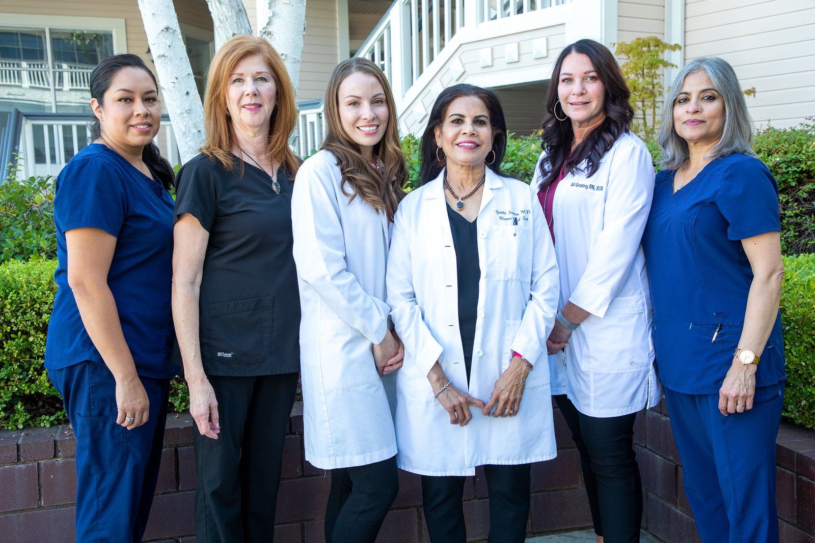 Alamo MD MedSpa team Six healthcare workers pose outside; all wearing scrubs or white coats.