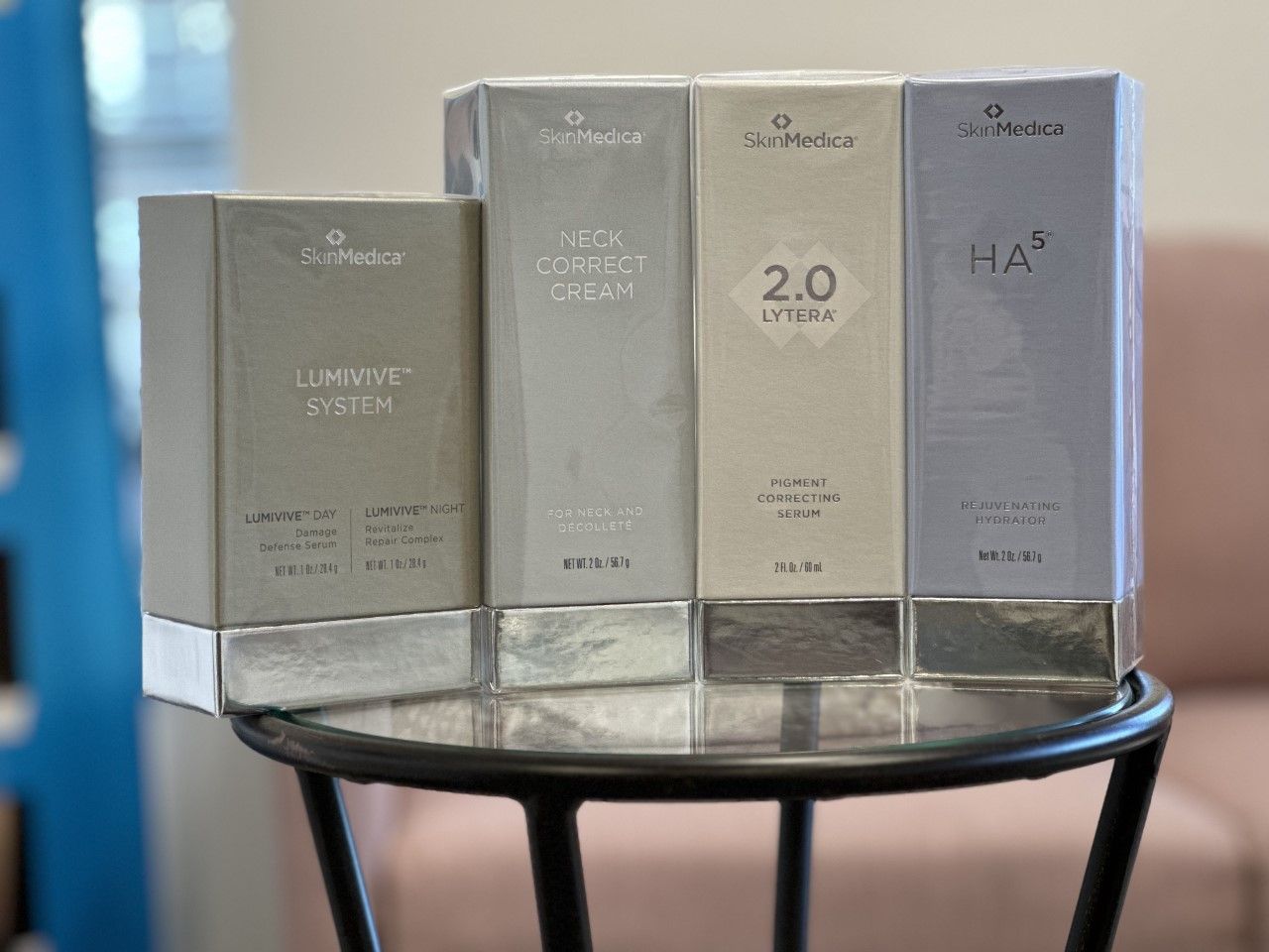Four skincare product boxes displayed on a black stool. The boxes are gray, white and silver.