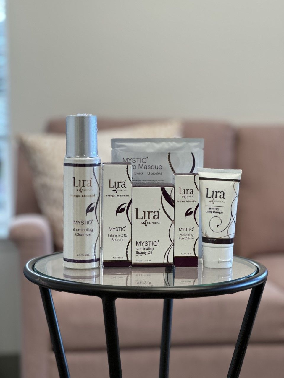 Assortment of Lyra products on a glass table. Includes bottles, tubes, and a mask, with a pink sofa in the background.