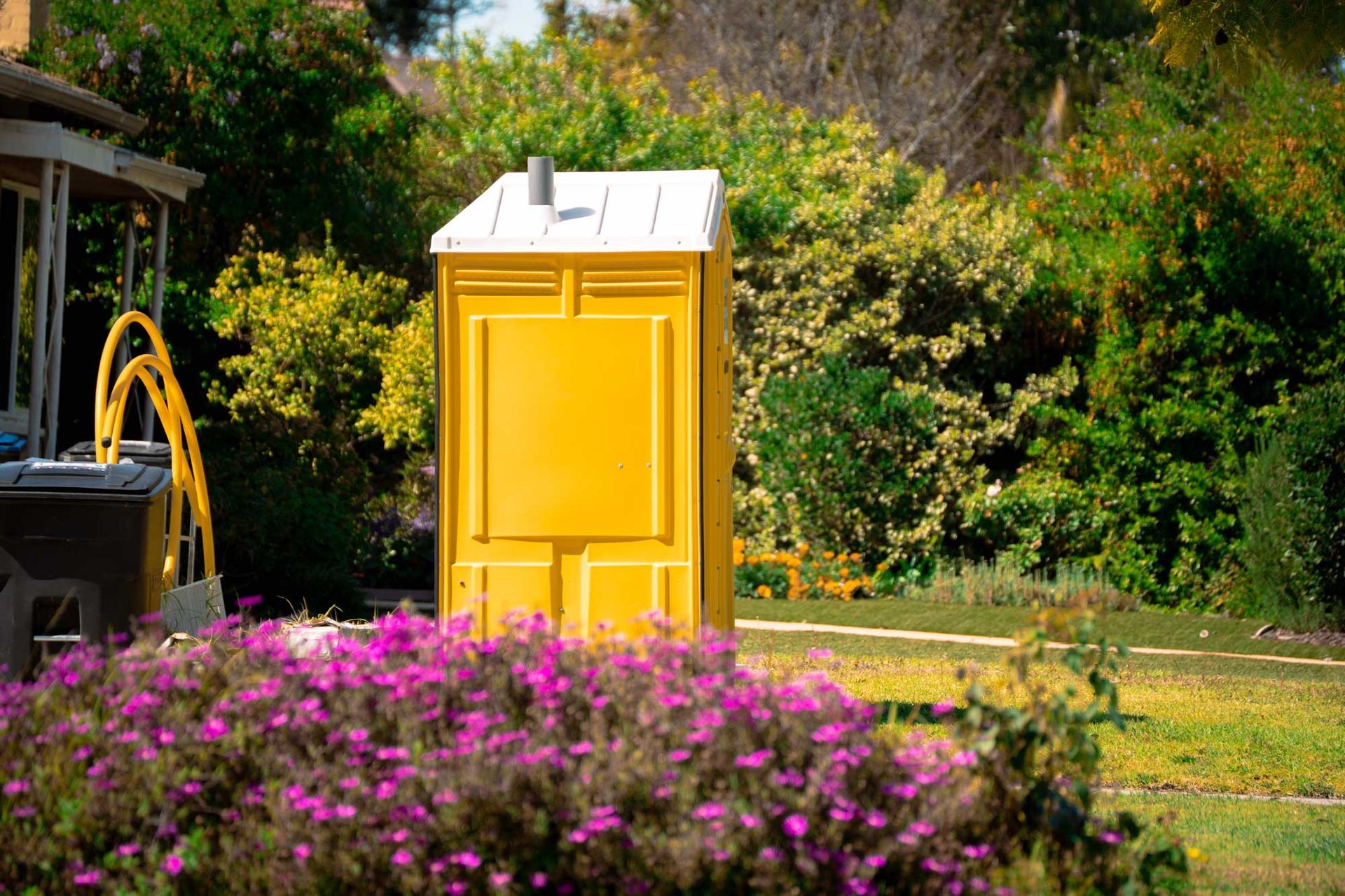 Bright yellow portable restroom unit set up in a lush green garden with blooming flowers. Bright yellow portable restroom unit set up in a lush green garden with blooming flowers.