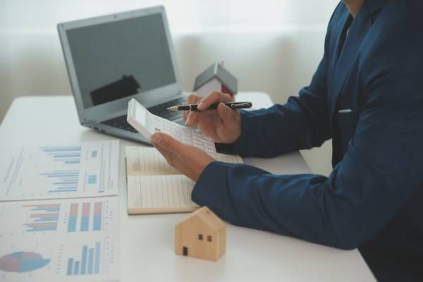 Person in blue suit reviewing documents at a desk with laptop and house model