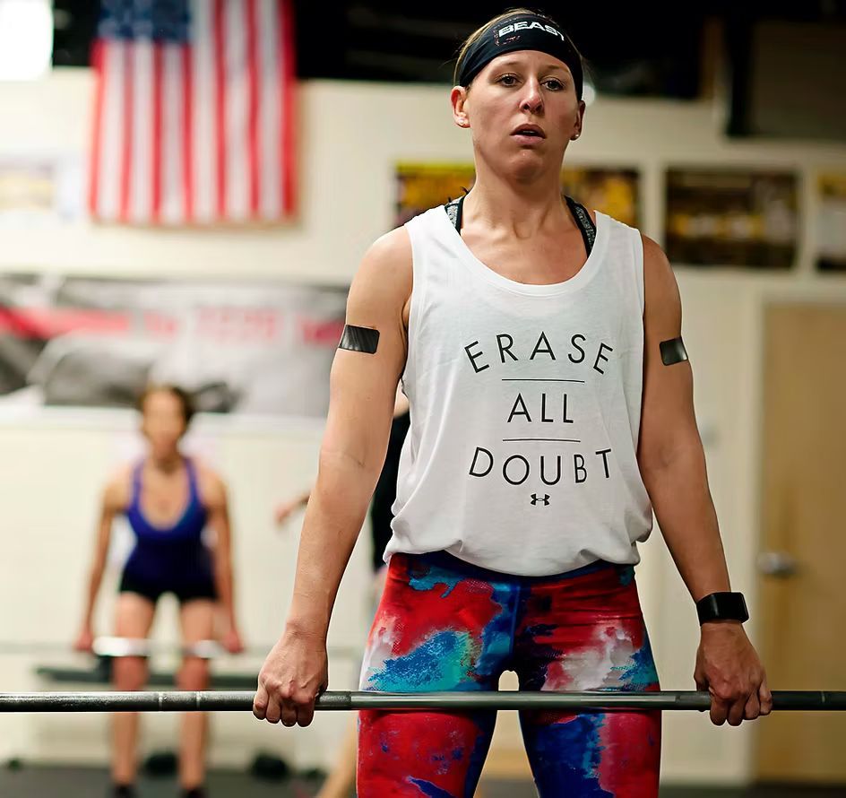 Woman lifting a barbell in a gym, wearing a tank top with