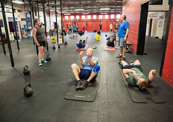 People exercising in a gym, doing sit-ups and other exercises. Black floor, kettlebells, red walls.
