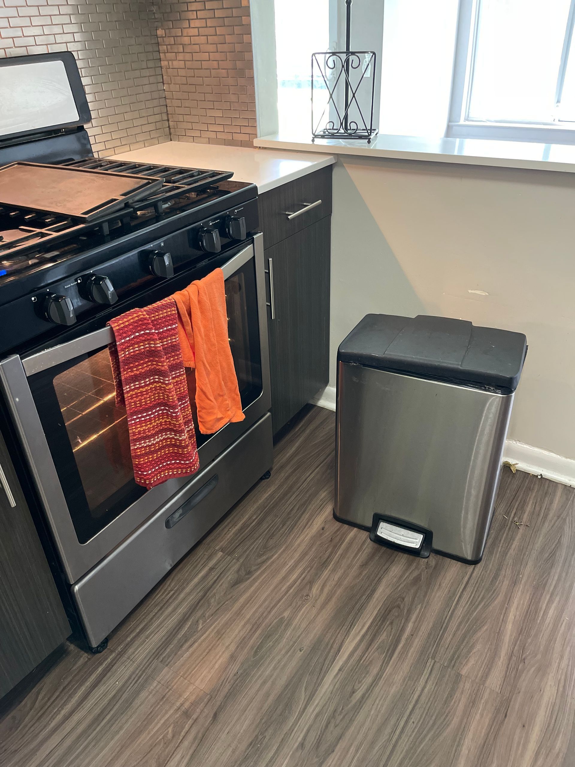 A kitchen scene featuring a black oven with two towels hanging on the handle next to a stainless steel trash can.
