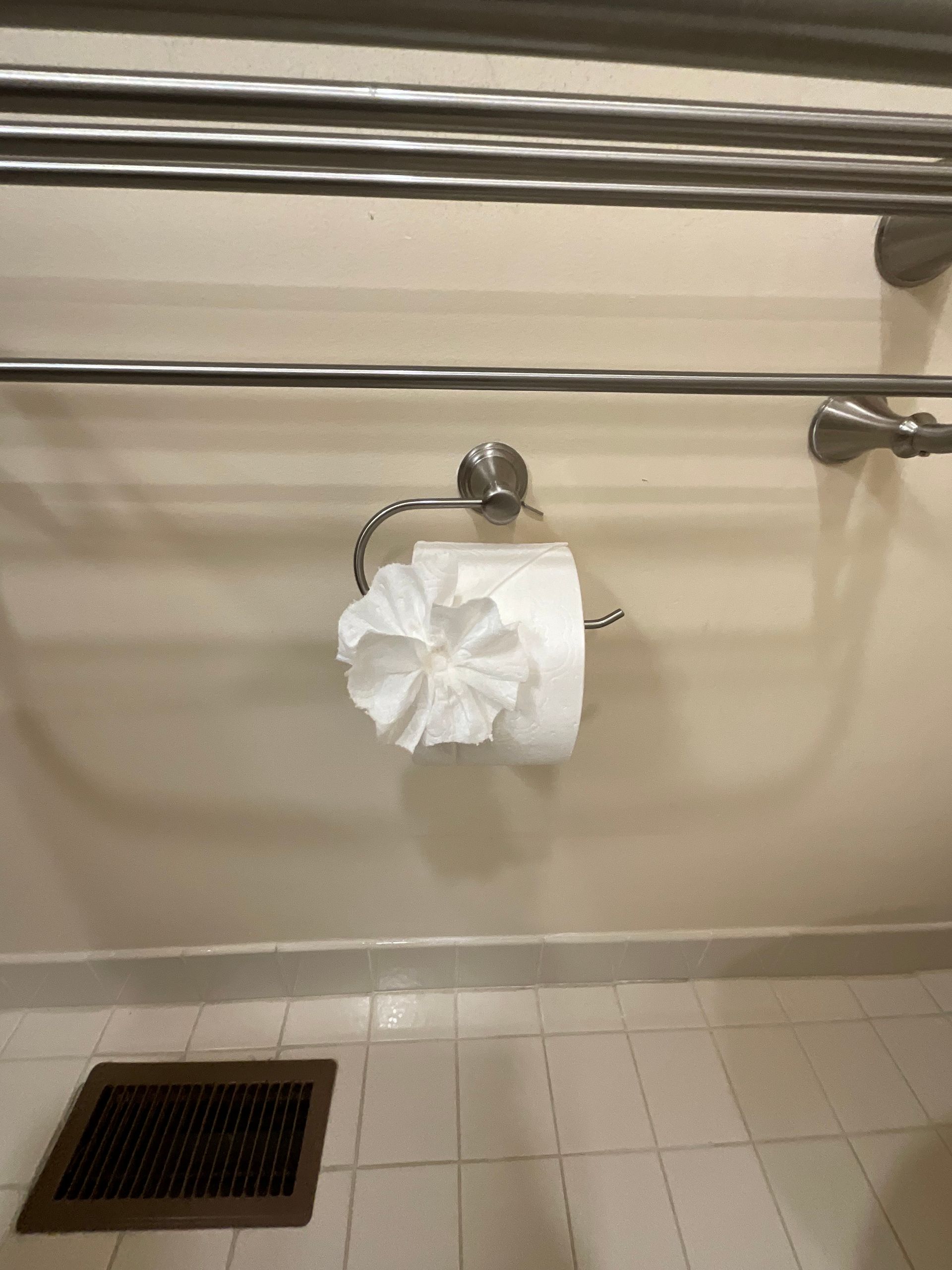 Toilet paper on a holder folded into a flower shape, mounted on a wall above a tiled floor.