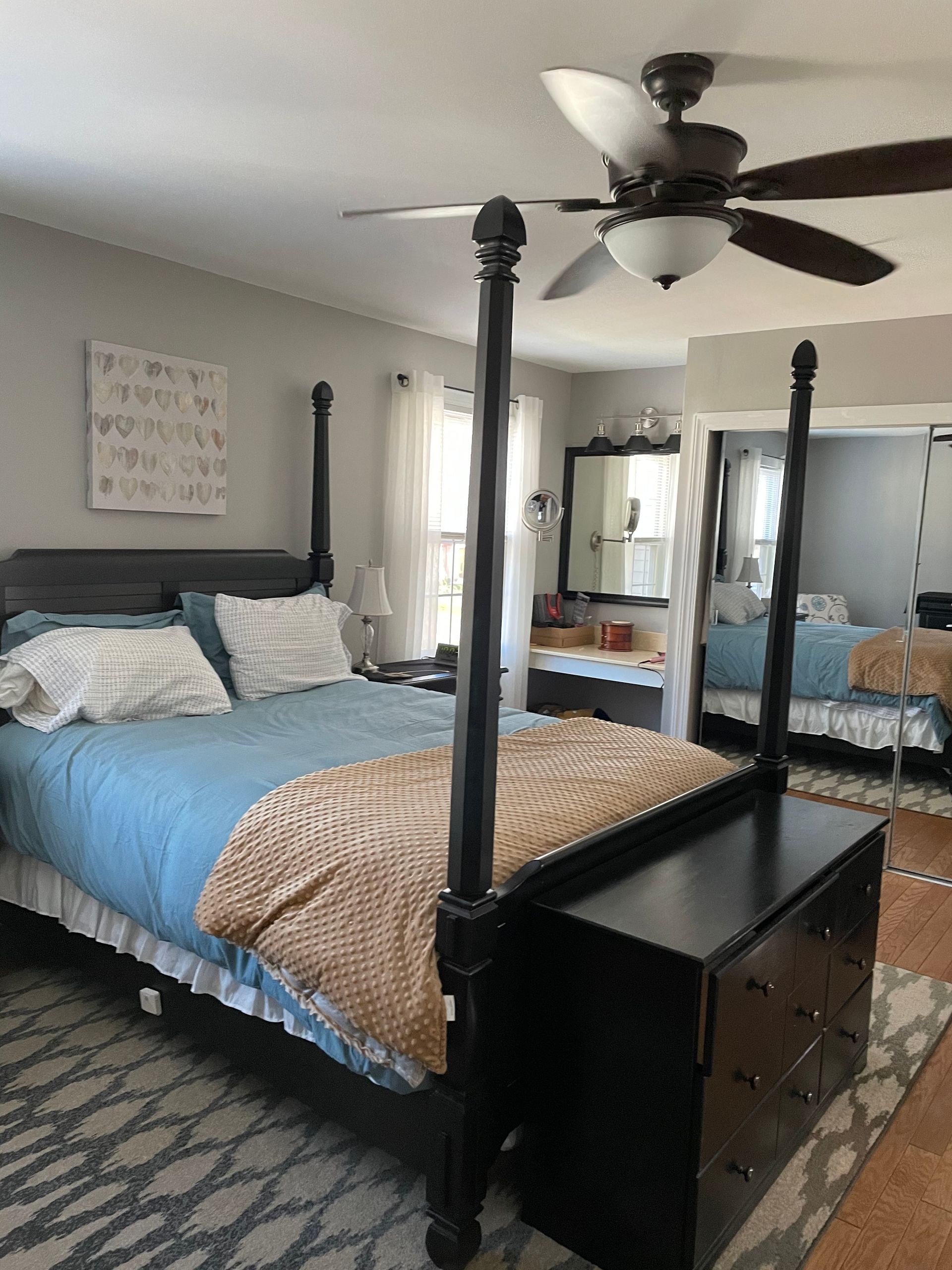 A bedroom featuring a black four-poster bed with blue bedding, a tan throw blanket, and a matching black wooden chest.