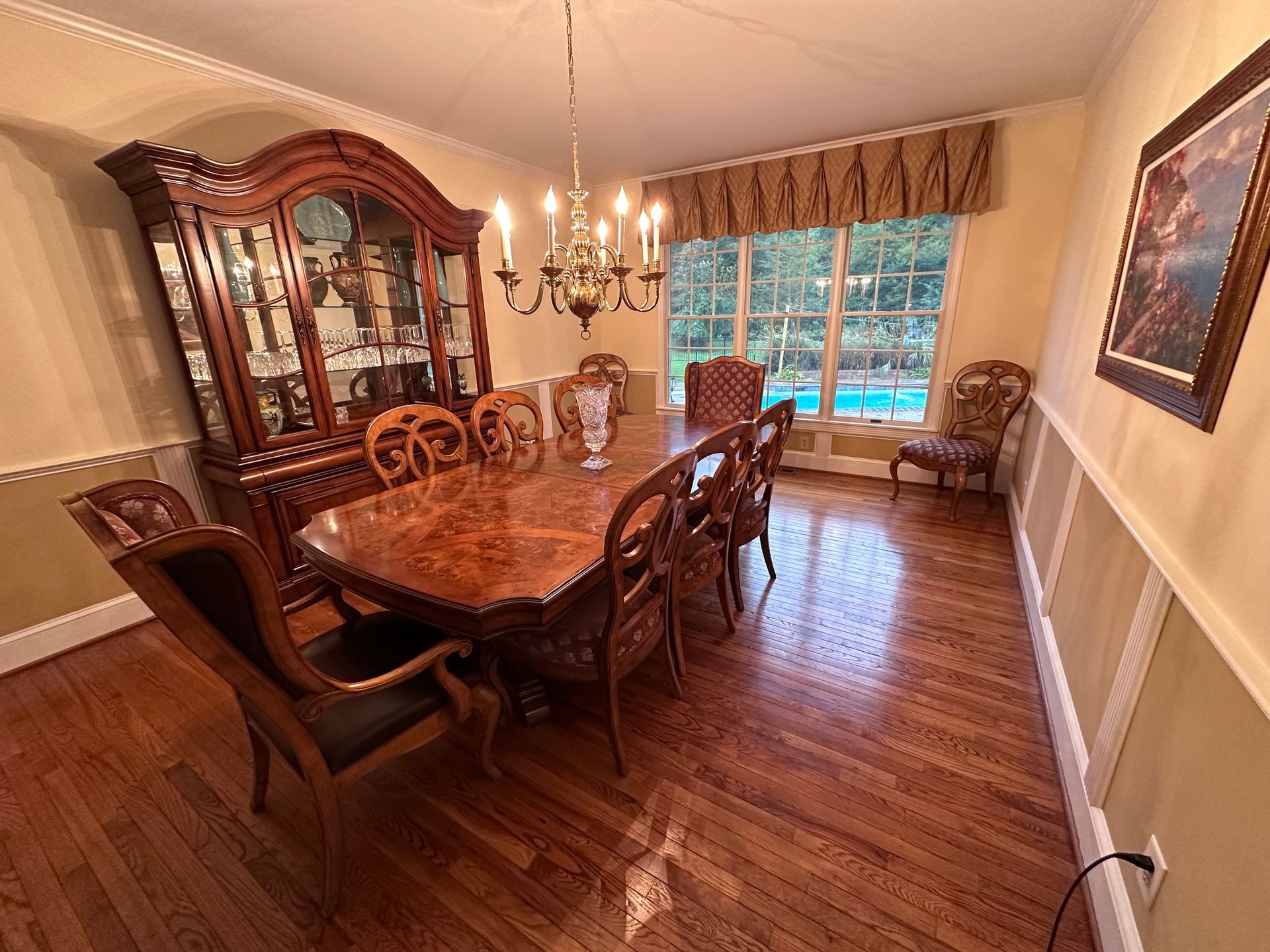 A formal dining room features a dark wood table, matching chairs, a large china cabinet, and hardwood floors.