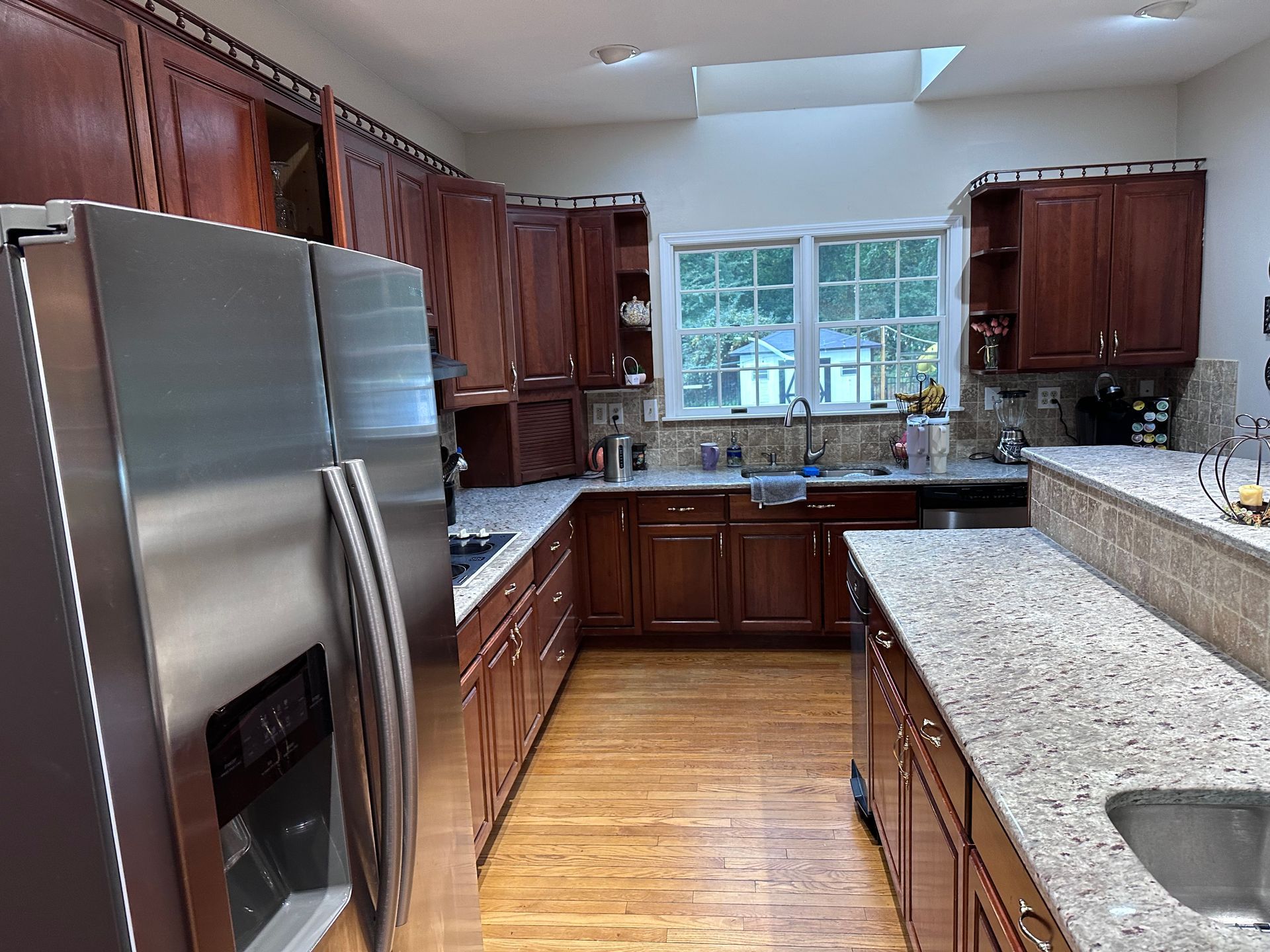 A kitchen featuring dark wood cabinets, speckled granite countertops, stainless steel appliances, and wood flooring.
