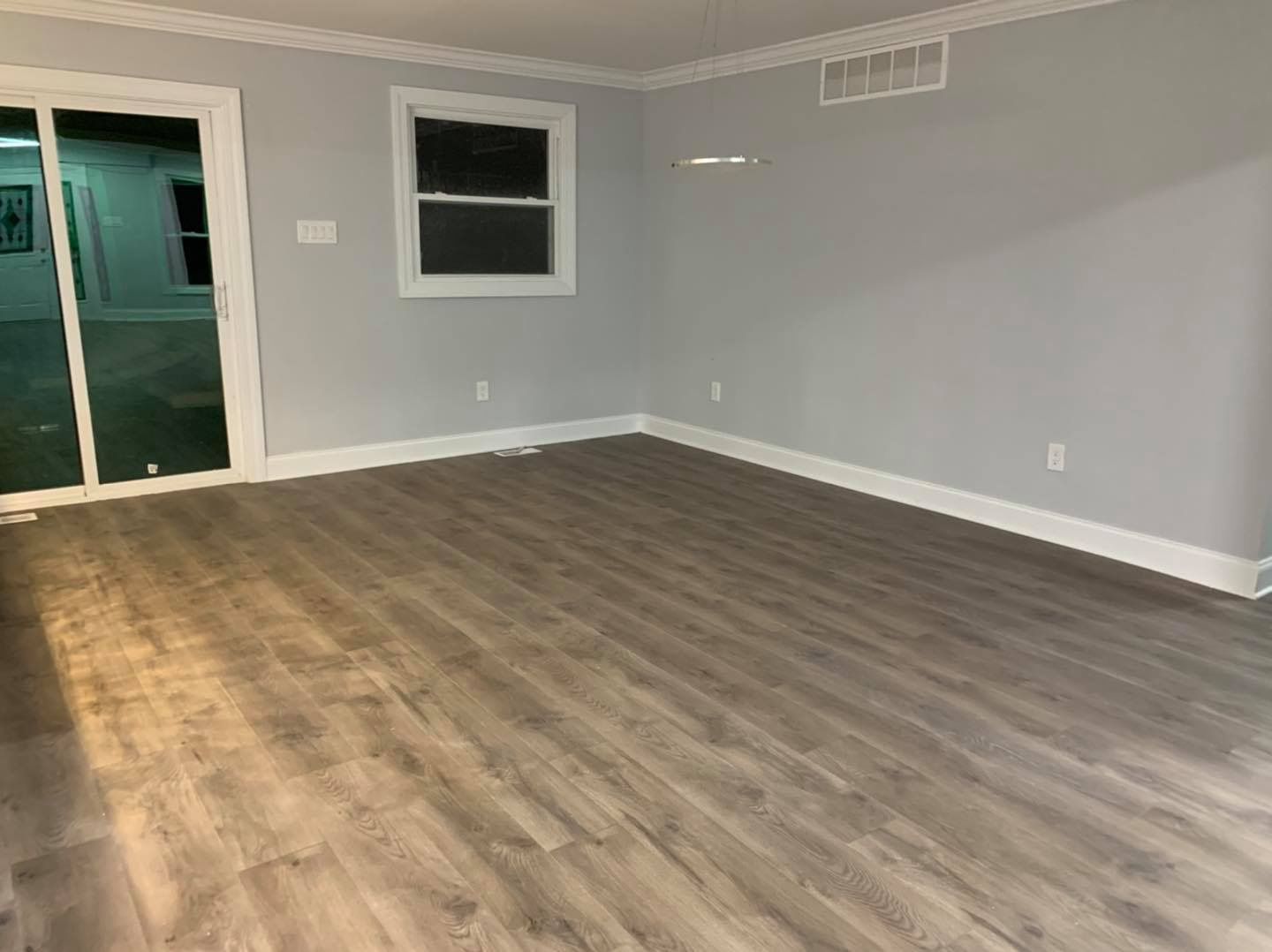 An empty room with light gray walls, white trim, wood-look flooring, a large sliding glass door, and a single window.