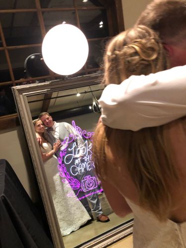 A bride and groom are posing for a picture in front of a mirror me Photo Booth