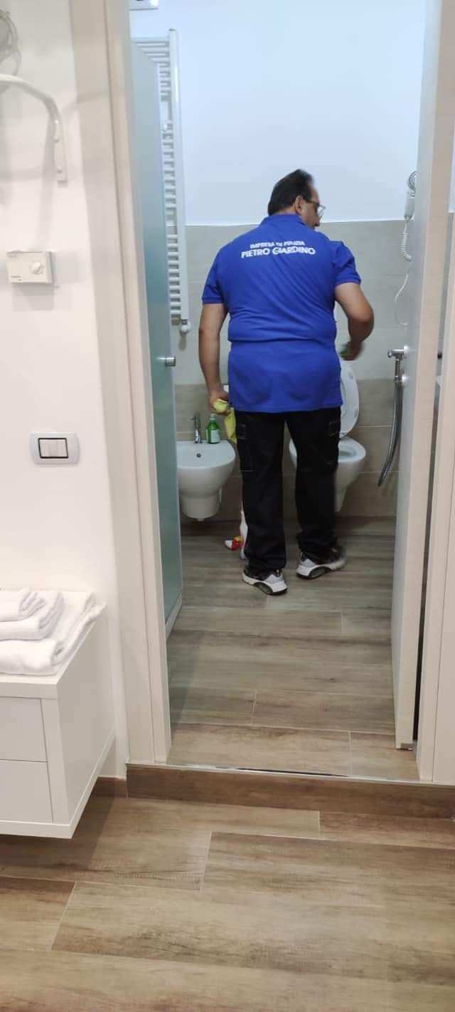 Un uomo con una camicia blu sta pulendo un bagno con uno straccio.