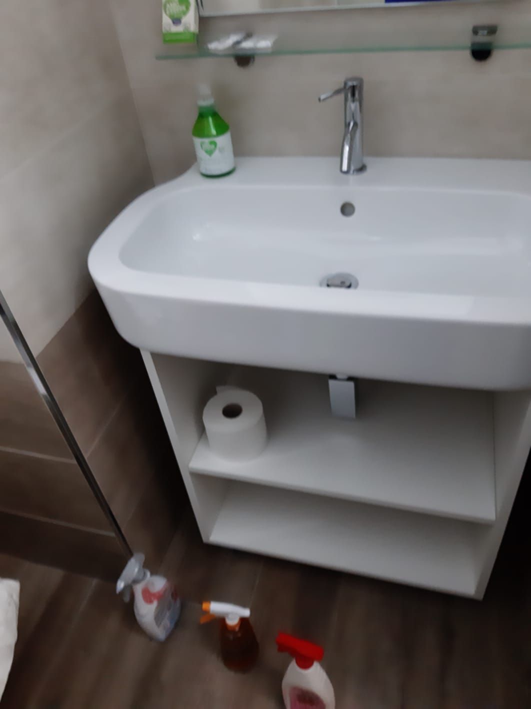 Un bagno con un lavandino, carta igienica e flaconi spray sul pavimento
