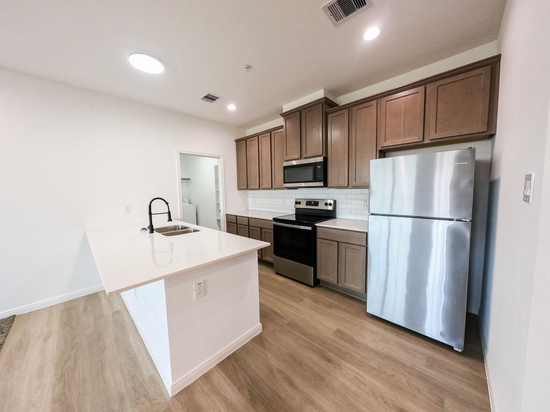Kitchen with island, stainless steel appliances, brown cabinets, and light wood floors.