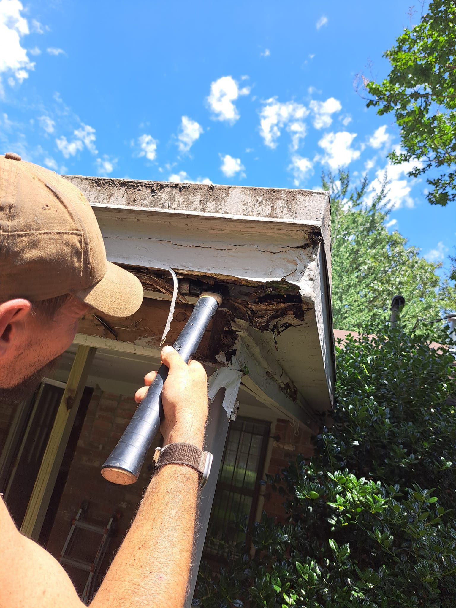 Person cleaning a white roof gutter with a brush under a blue sky