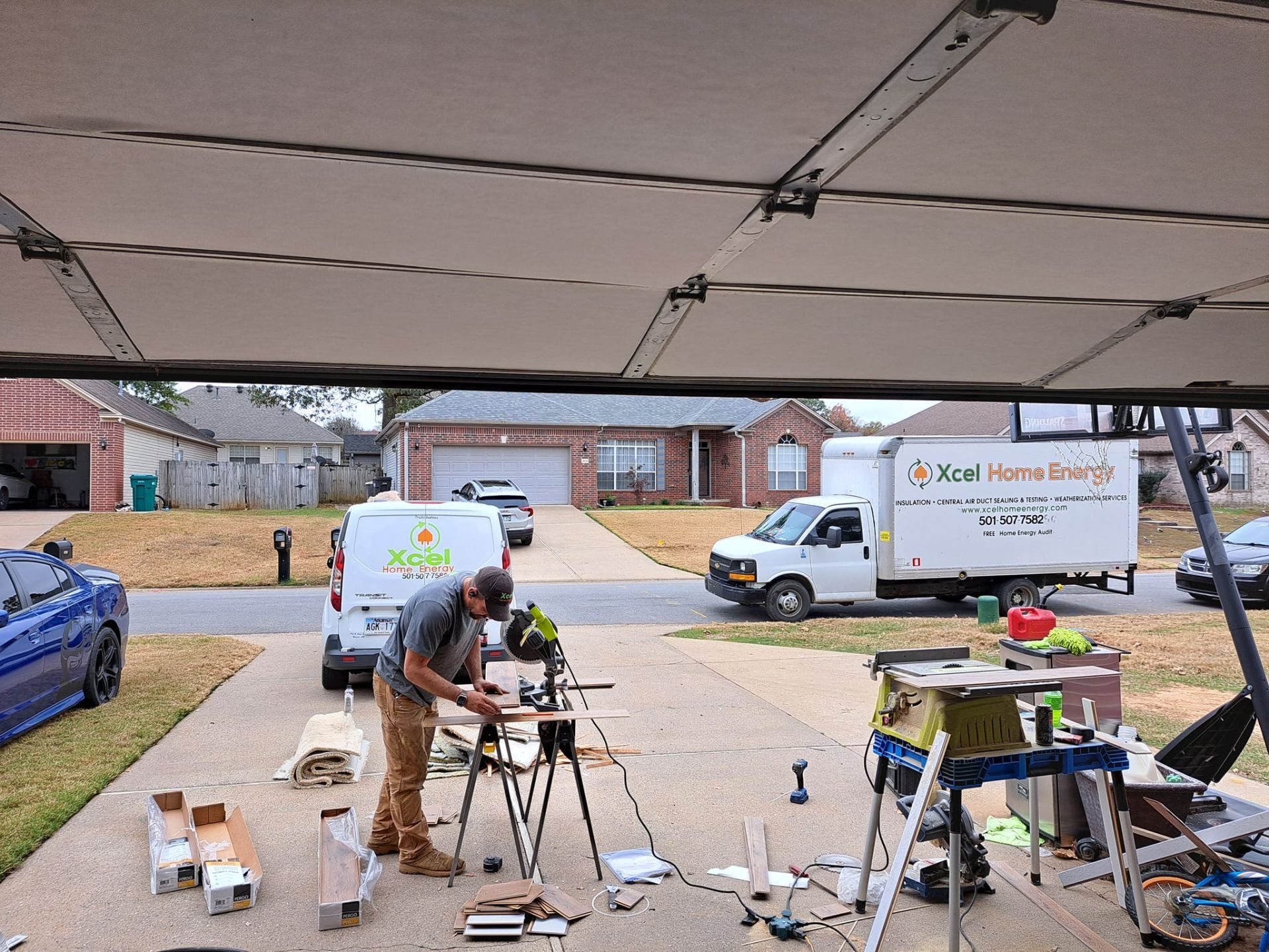 People working on equipment under a carport, with vans and tools in a driveway.